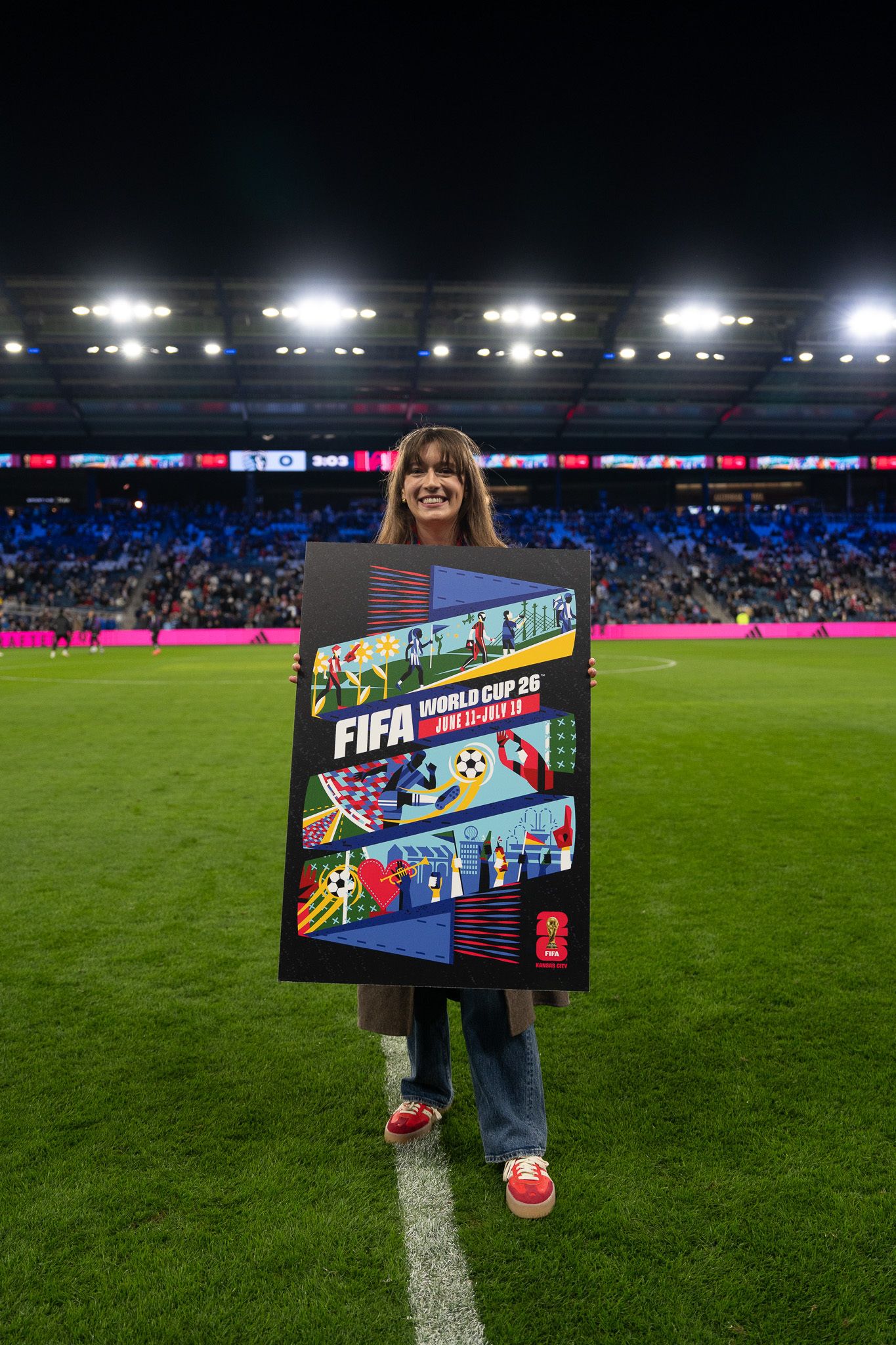woman stands holding fifa poster on a soccer field