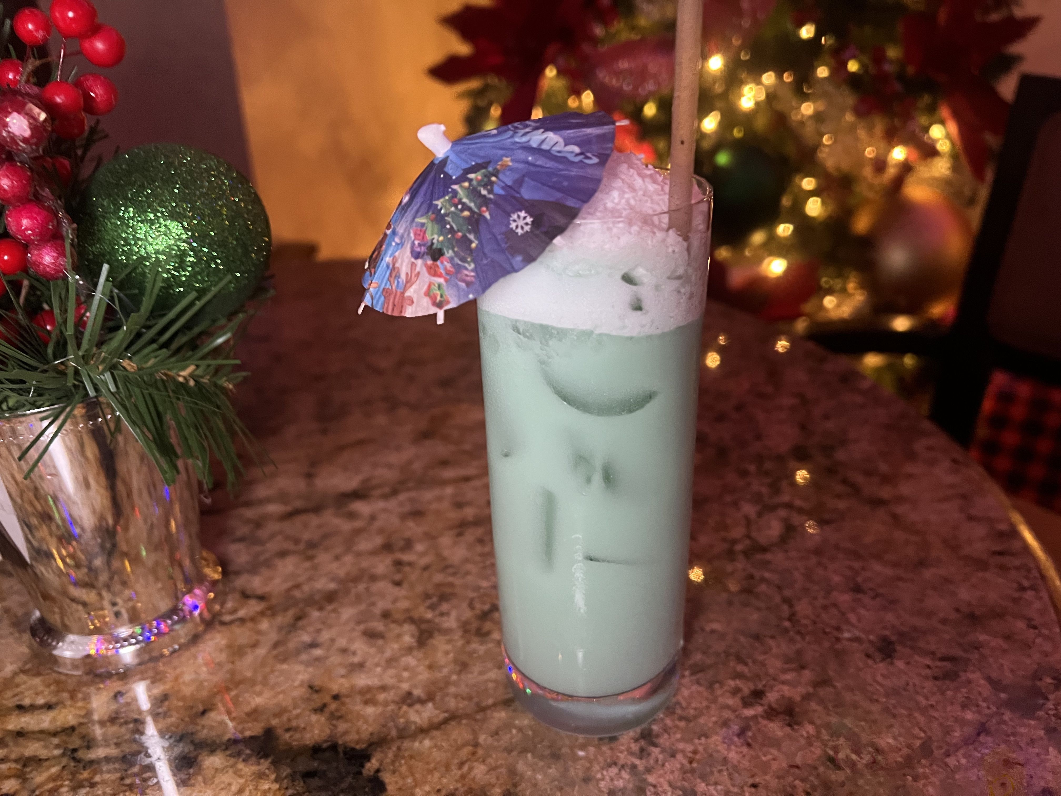 A tall cocktail glass filled with a light blue drink garnished with a small paper umbrella.