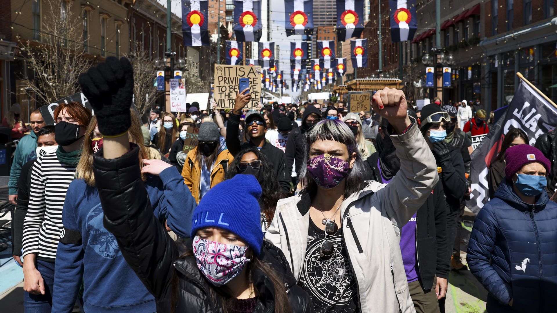 Two women stand in front of a crowd wearing face masks and beanies