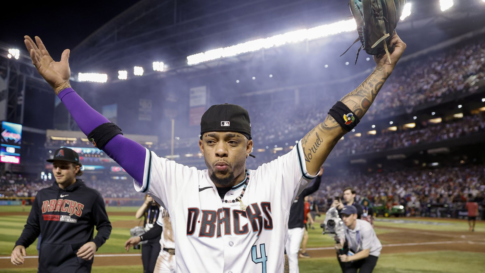 A baseball player walks off the field holding his arms up triumphantly. 