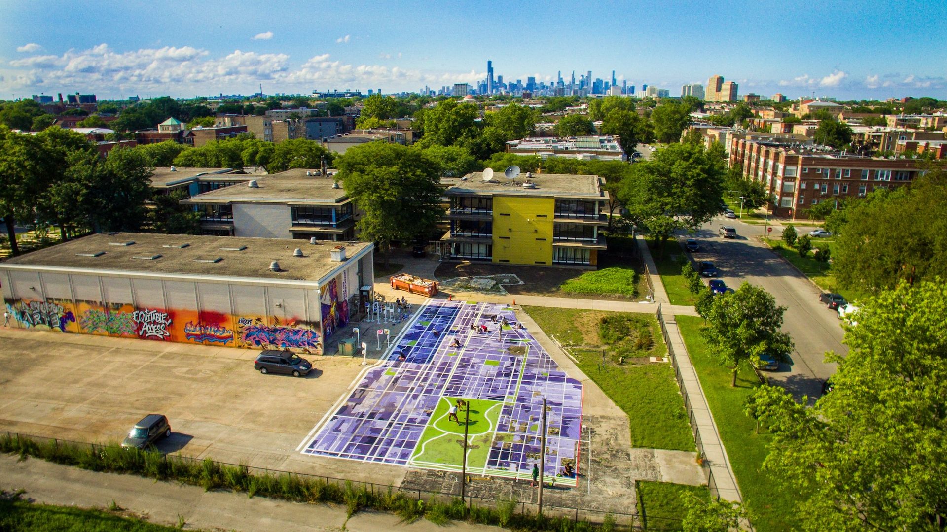 Aerial photo of a closed school with a painted map of Chicago on the parking lot with the Chicago skyline in the background.