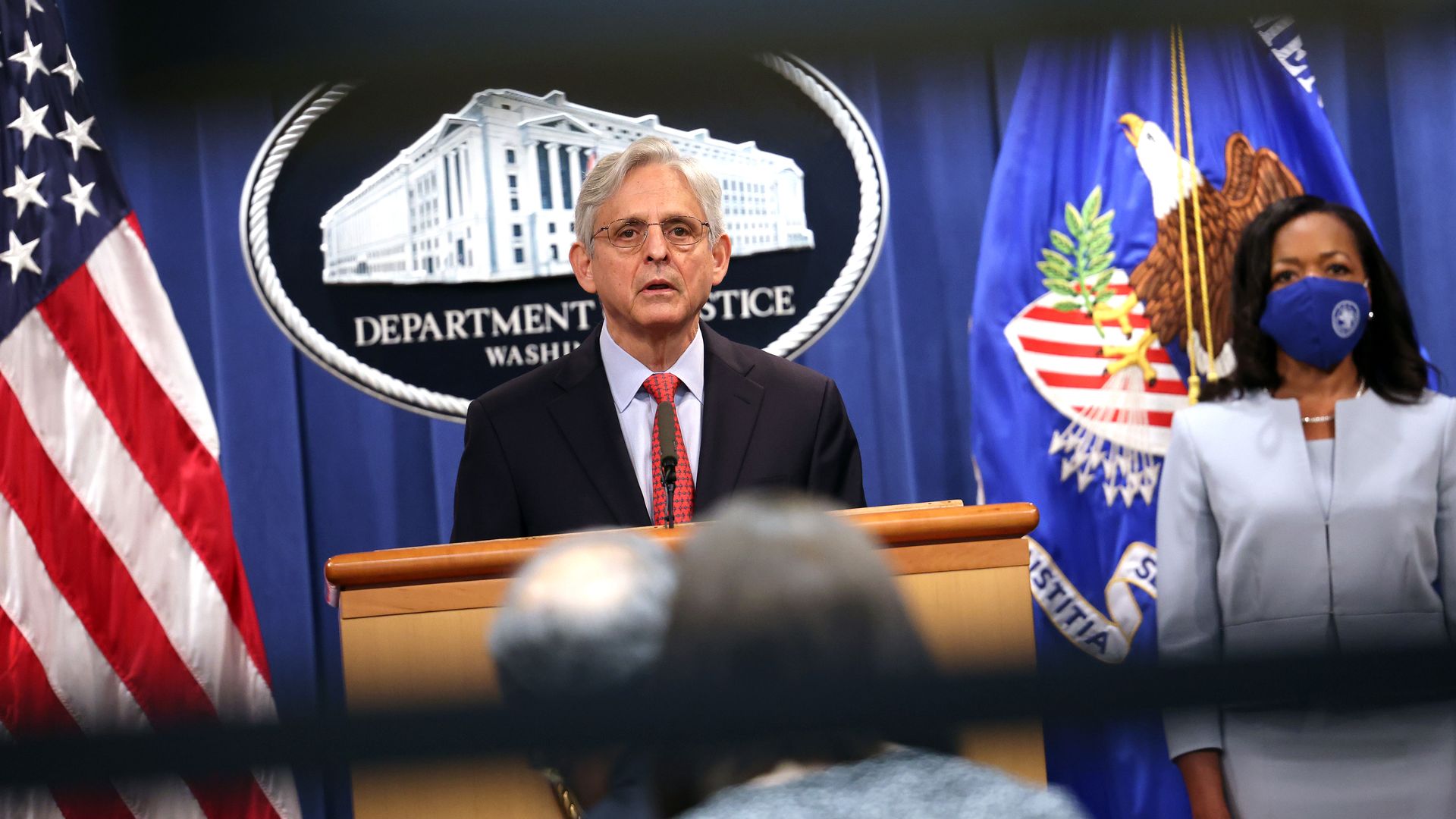 Photo of Merrick Garland speaking from a podium as Kristen Clarke stands behind him, masked