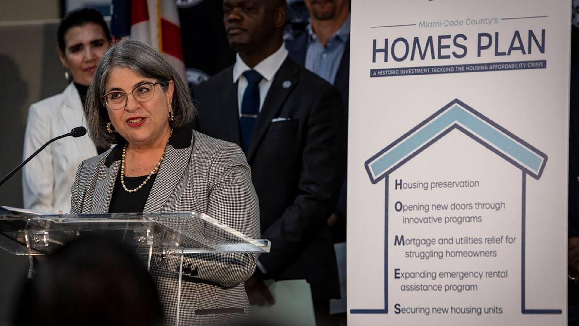 Miami-Dade County Mayor speaks at a podium while wearing a grey checkered blazer.