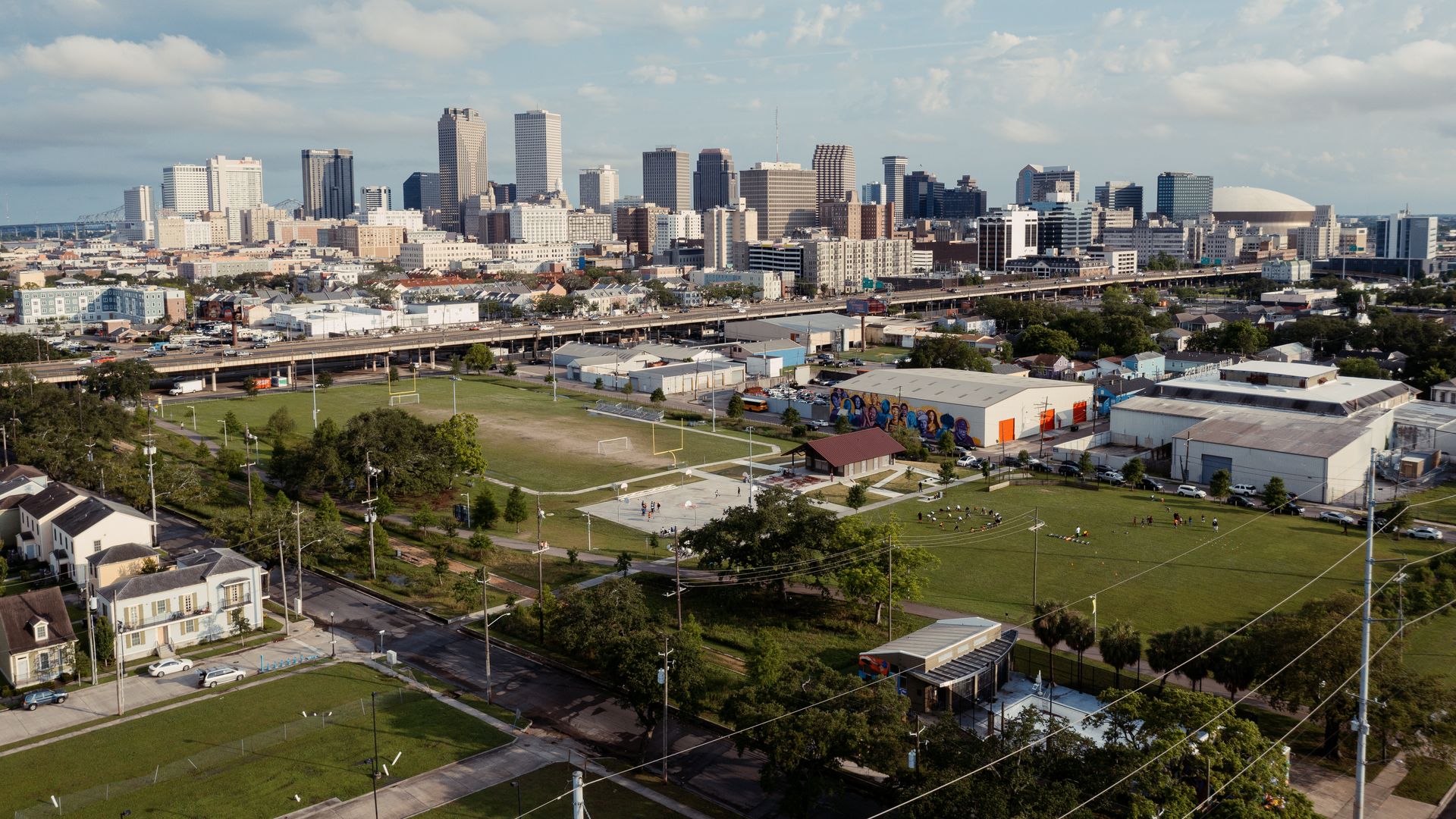 An aerial view of a greenspace and warehouses with the New Orleans skyline behind it.