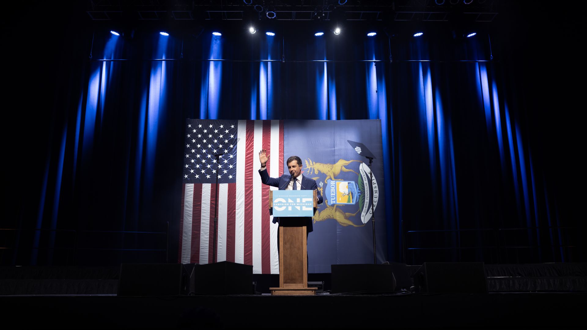 Buttigieg stands in front of the American and Michigan flags.
