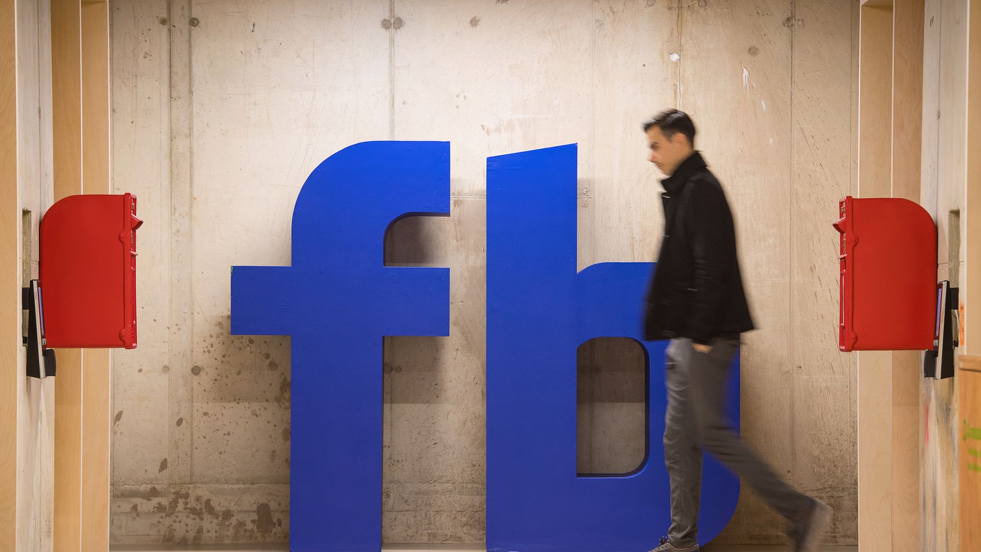A man walks by a giant Facebook logo