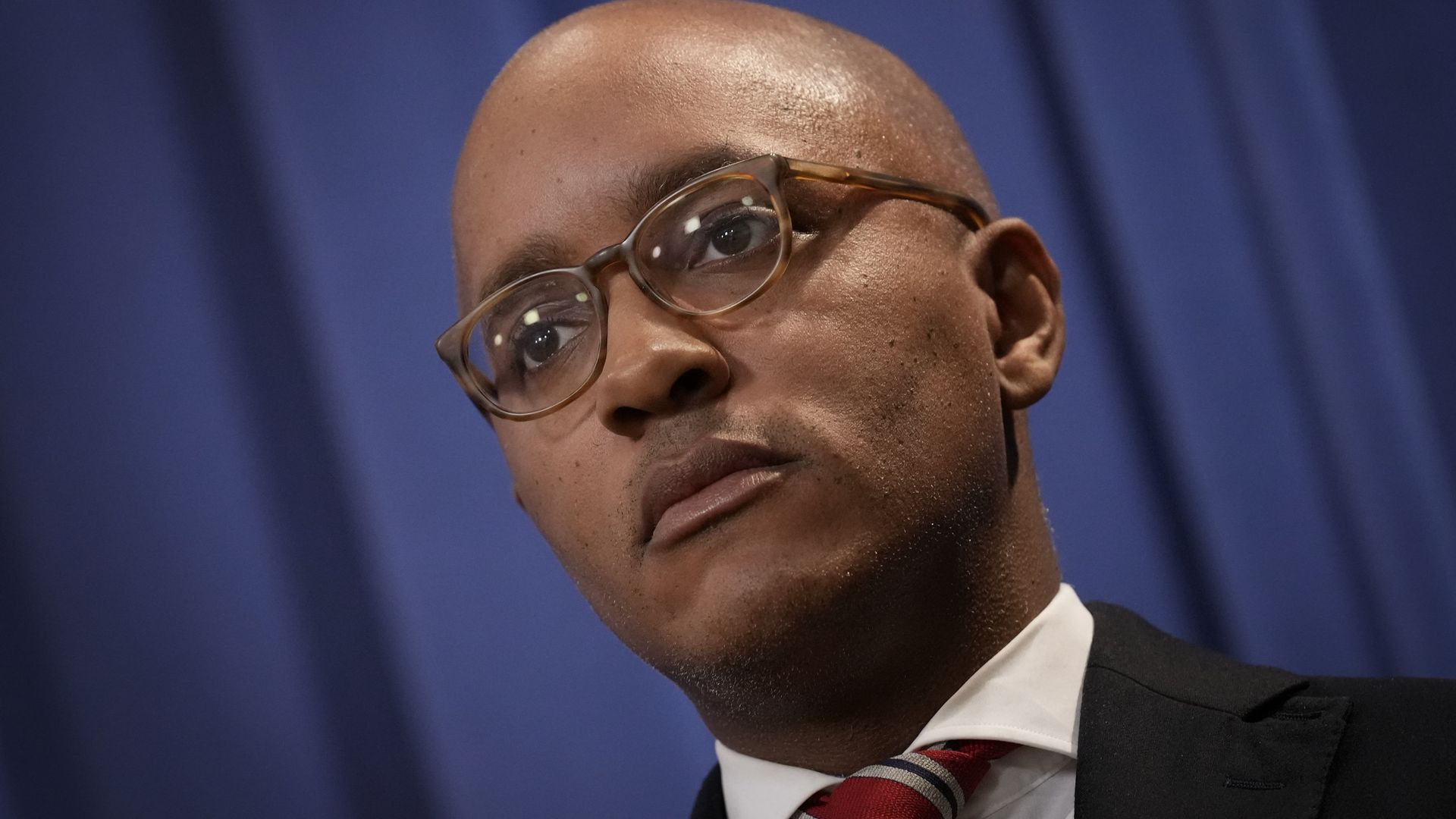 Face of an African-American man waiting to speak at a news conference, in a business suit.