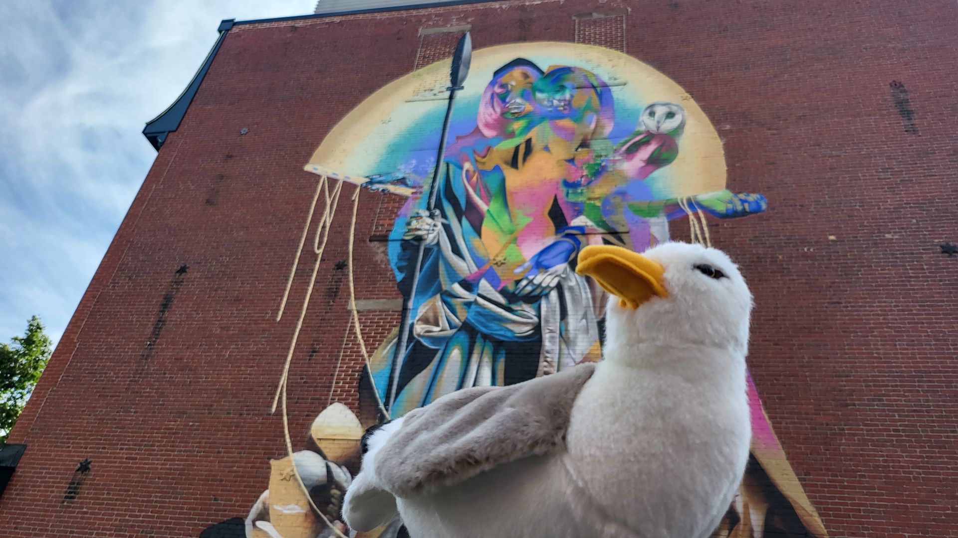 A plush seagull in front of a large mural of Athena.
