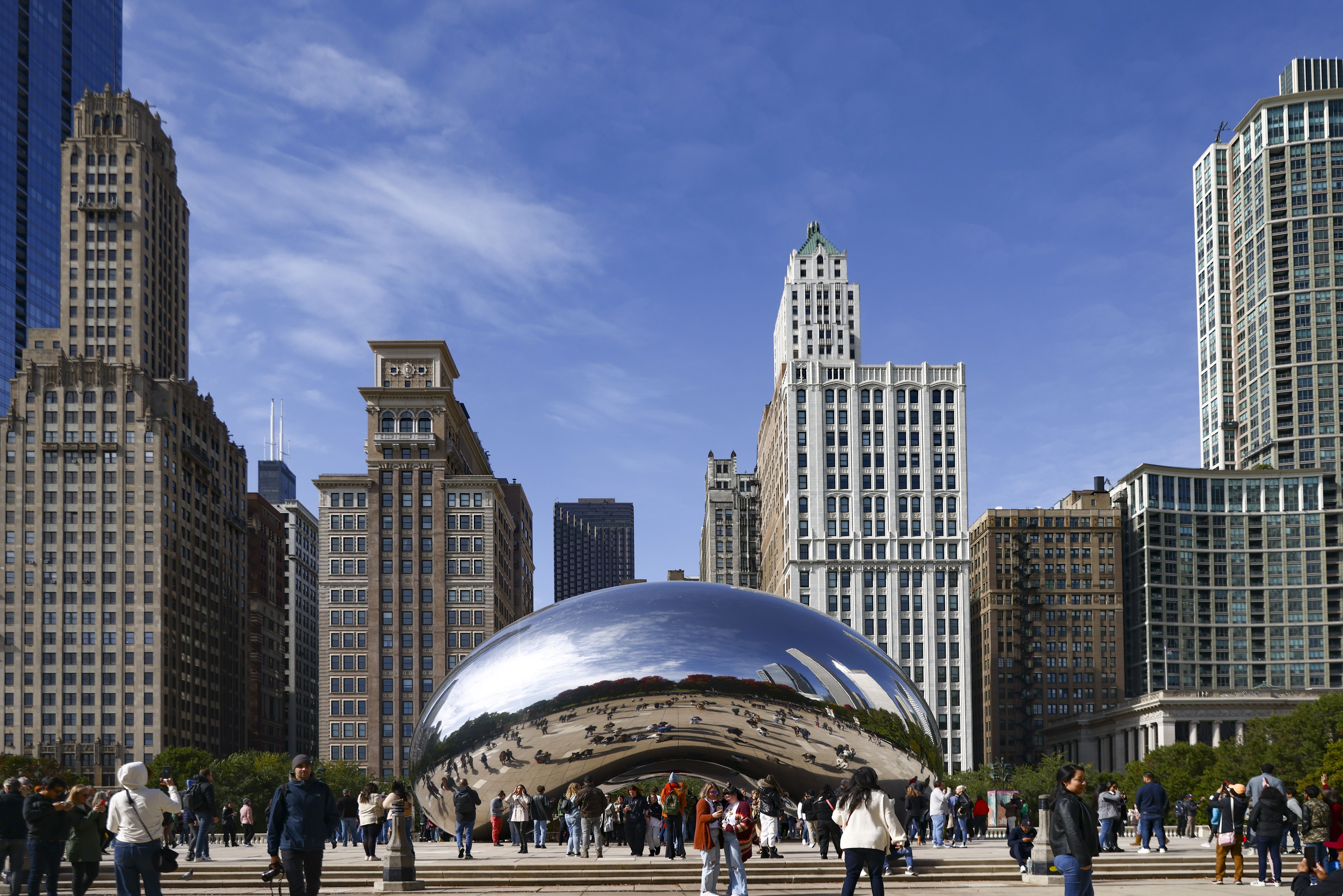 The "Cloud Gate" sculpture, also known as The Bean, is surrounded by tourists with Chicago's skyline in the background.