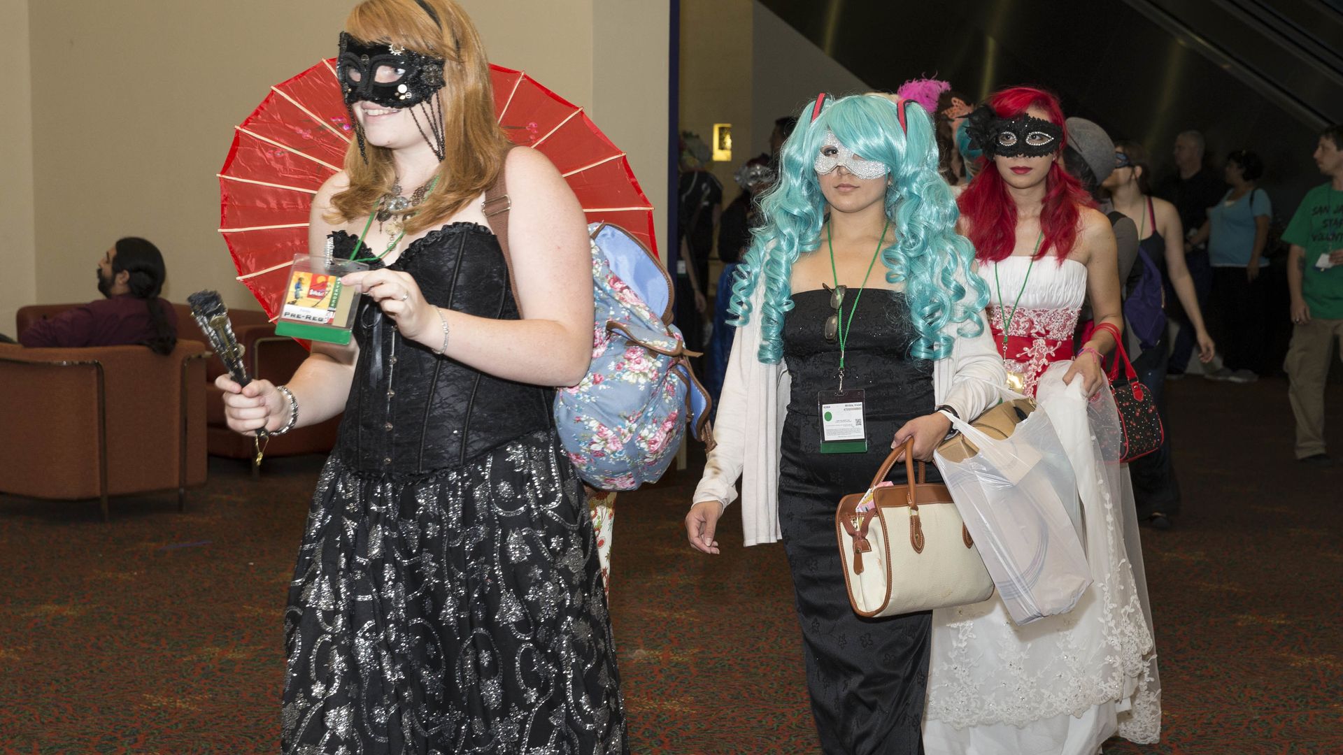 Three San Japan guests dressed in cosplay outfits walk in a line through a convention center space.