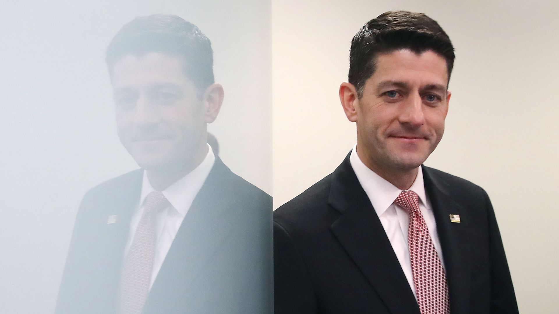 In this image, Paul Ryan leans against a reflective white wall while wearing a suit and red tie. 