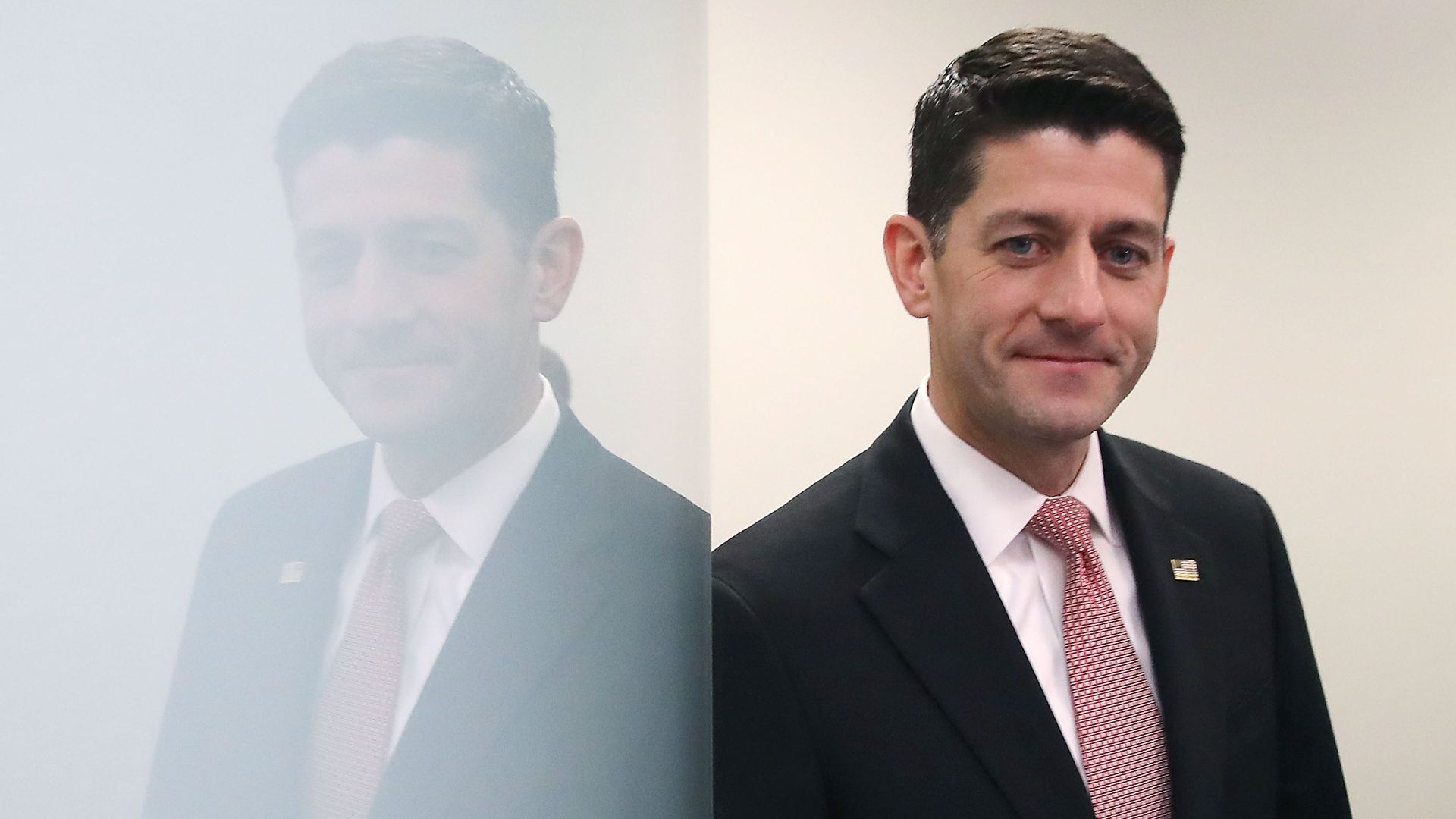 In this image, Paul Ryan leans against a reflective white wall while wearing a suit and red tie.