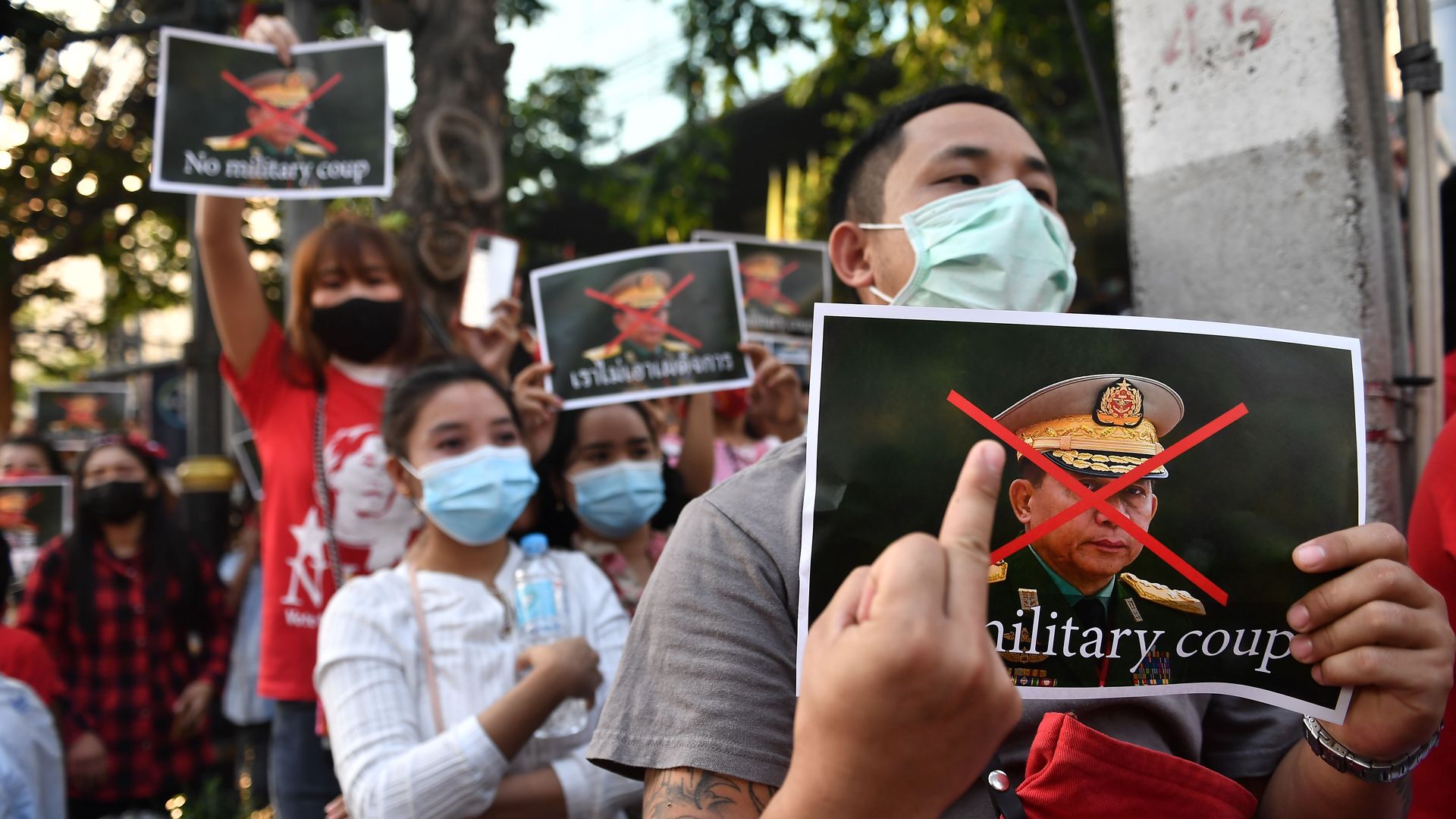 Photo of a protester holding their middle finger to a sign that says military coup
