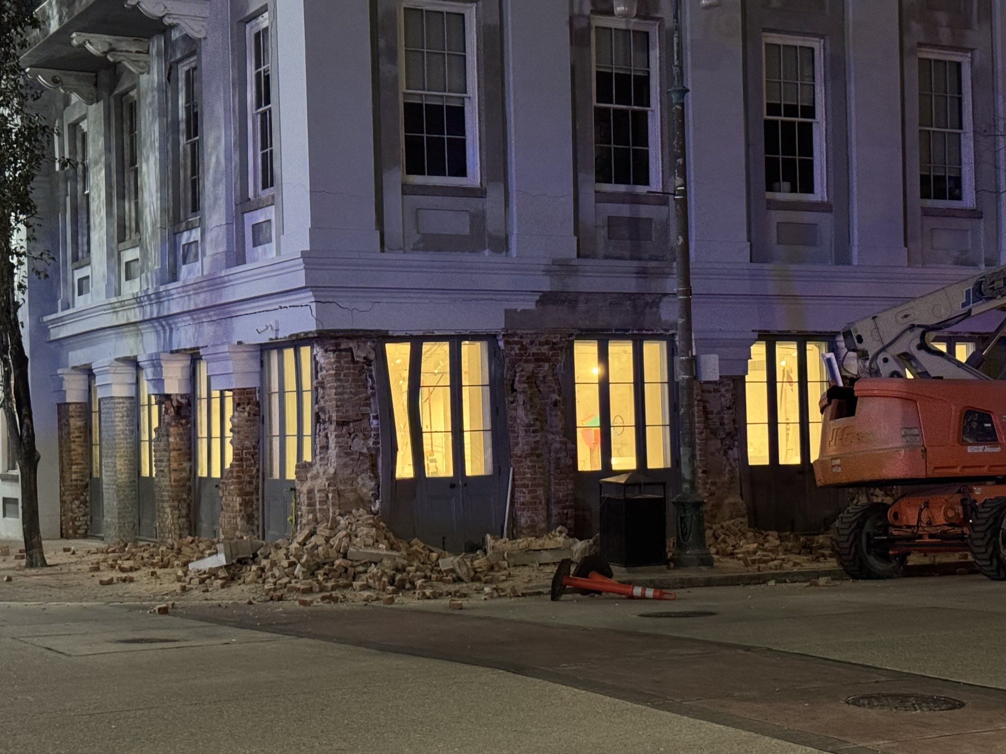A building is photographed at night. Bricks along the bottom of the building have partially spilled into the sidewalk around it.