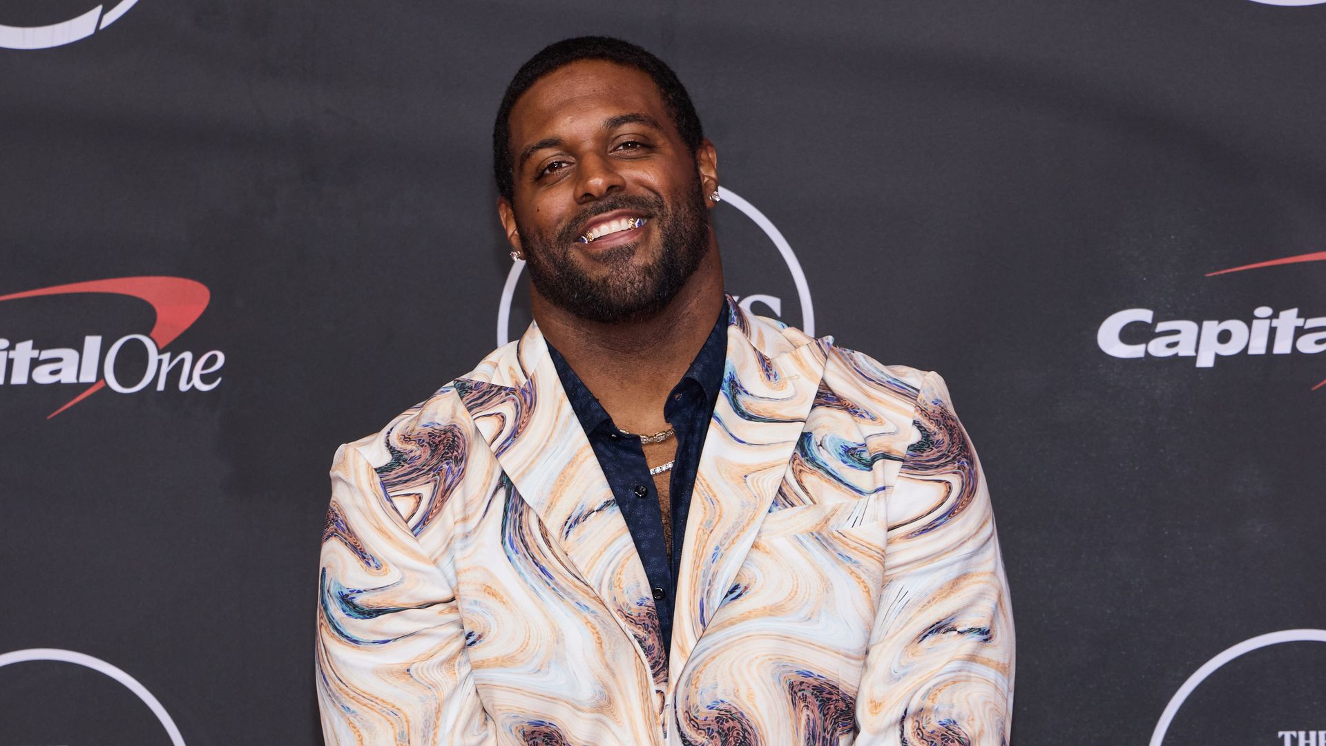 Image shows Cam Jordan smiling in a multi-colored suit.