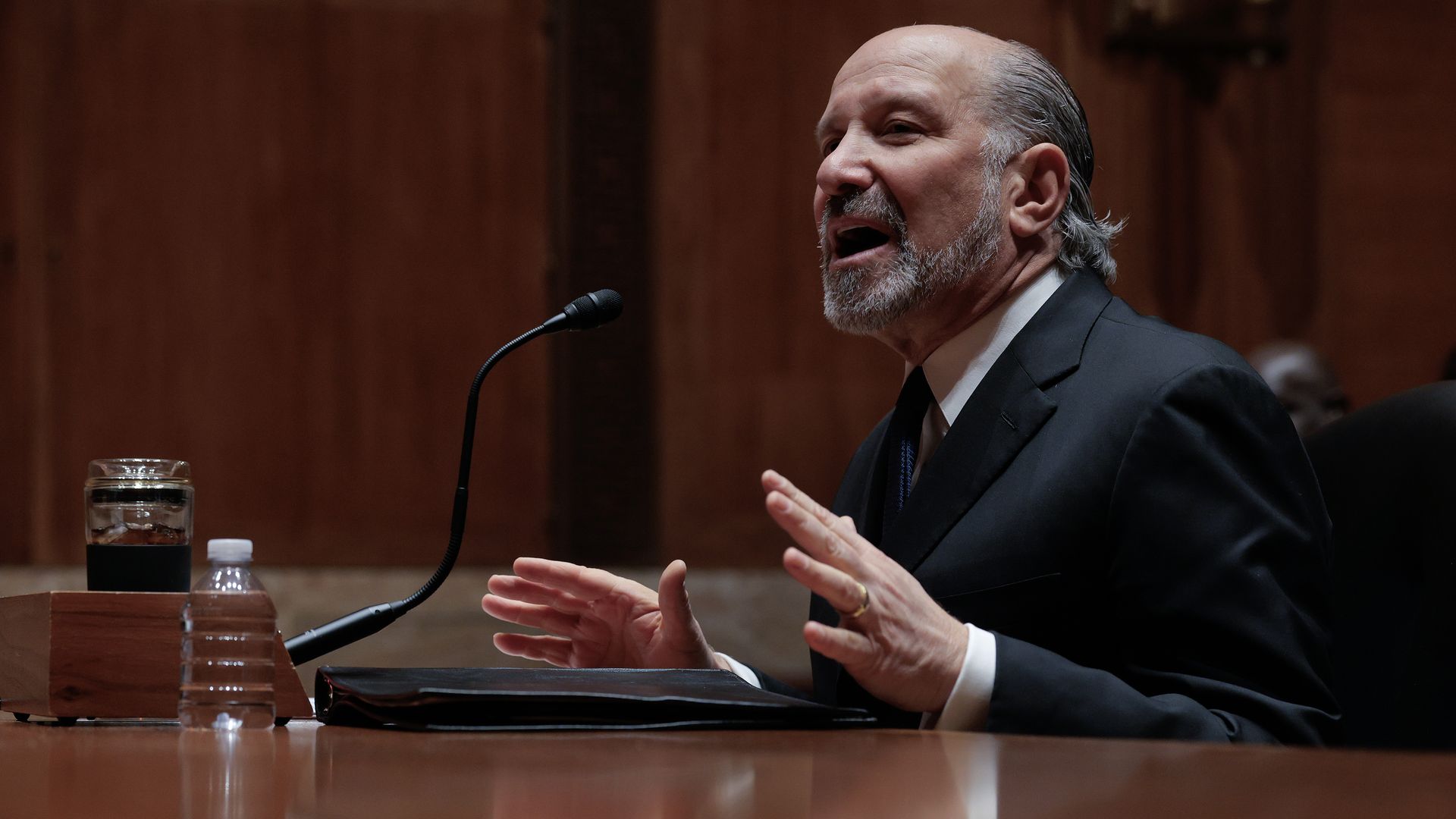 Howard Lutnick speaking into a microphone at a Senate hearing with lawmakers in the background.