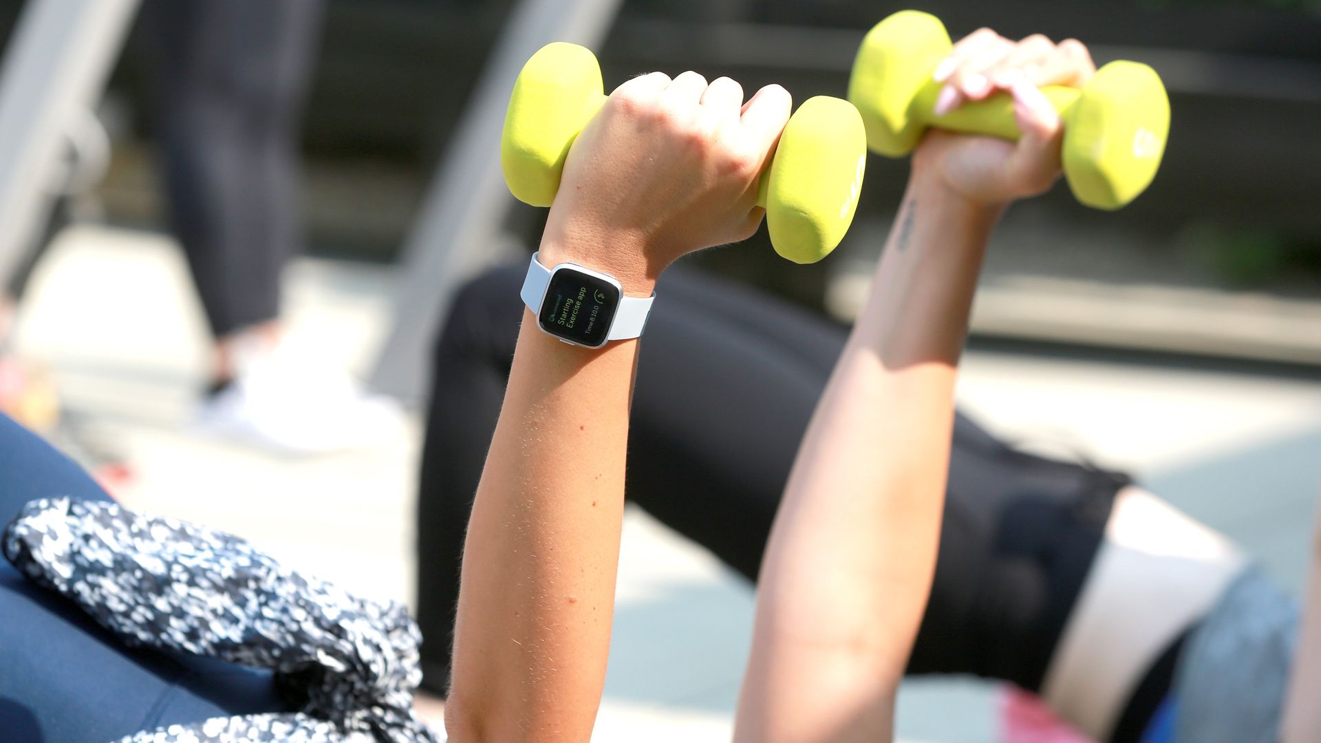 people holding dumbbells as they work out with a Fitbit fitness tracker