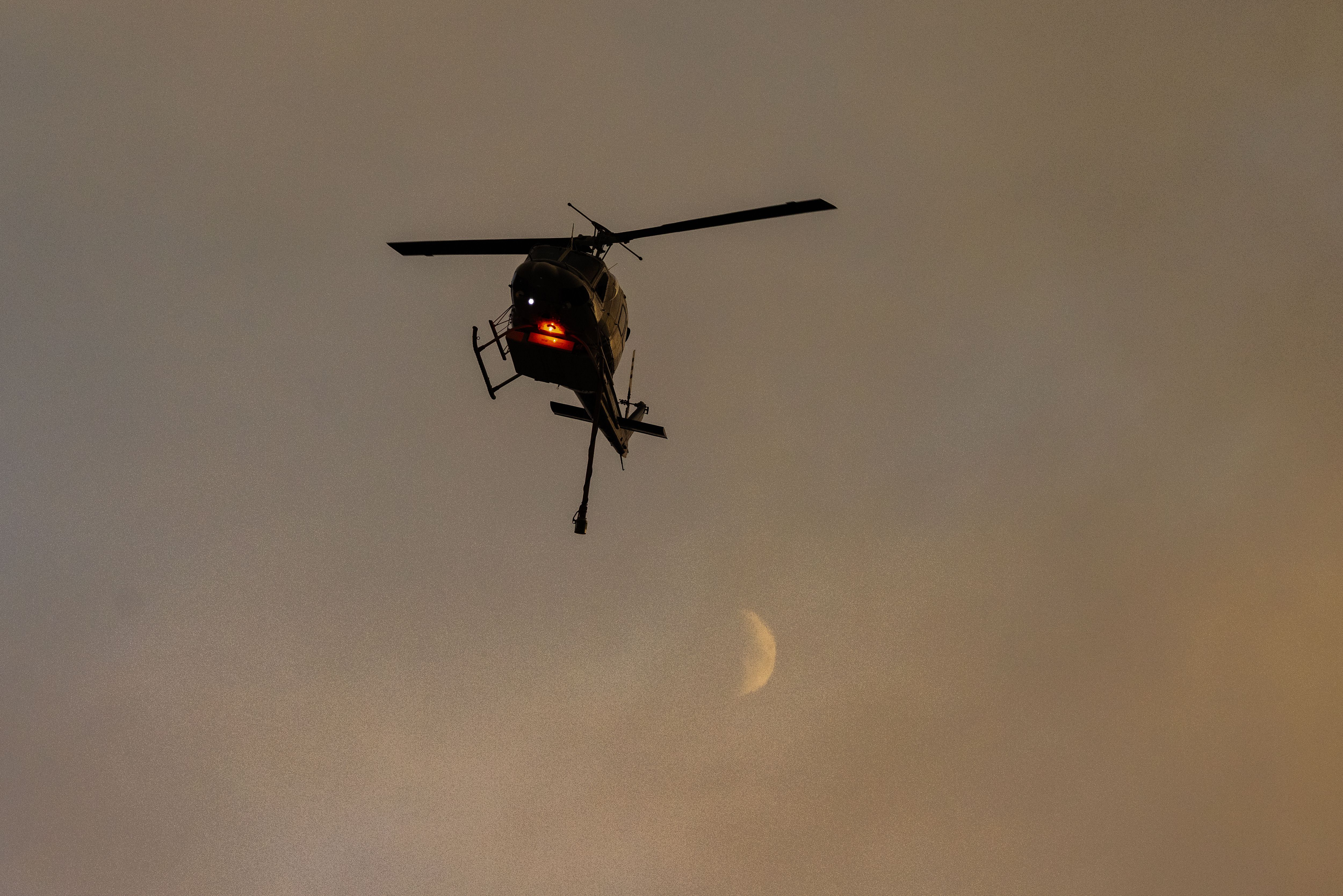 A firefighting helicopter and the moon are seen over the Bridge Fire near Glendora, California