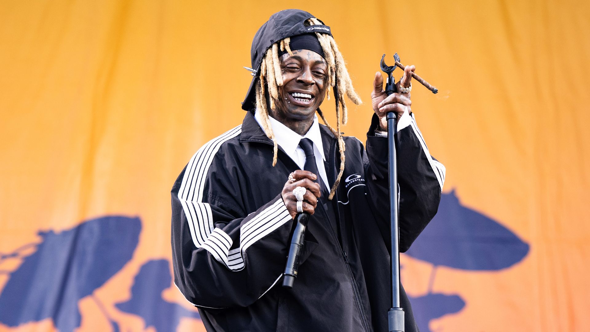 Lil Wayne holds a blunt in one hand and a microphone in the other while he smiles onstage.