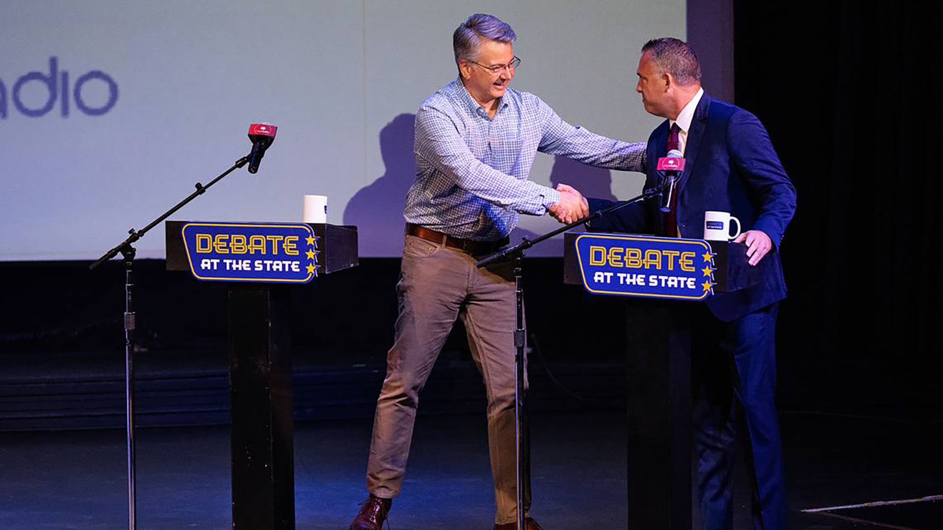 Rep. John Duarte shakes hands with Adam Gray while standing on a stage with two podiums.