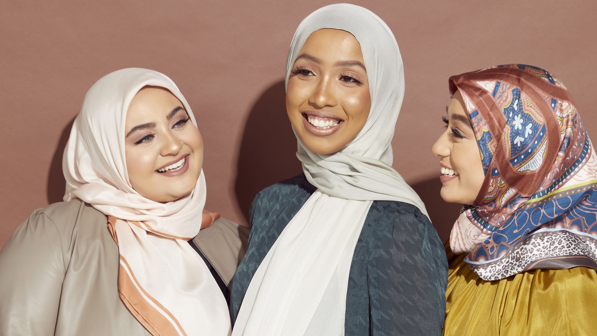 Three women wearing hijabs smile at one another.