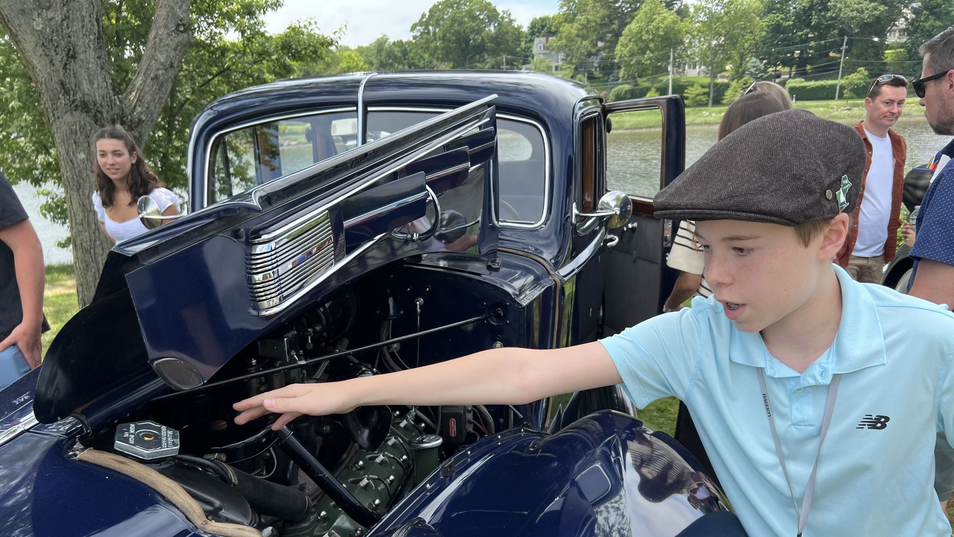 A teenage boy shows off the engine of an old Packard car.