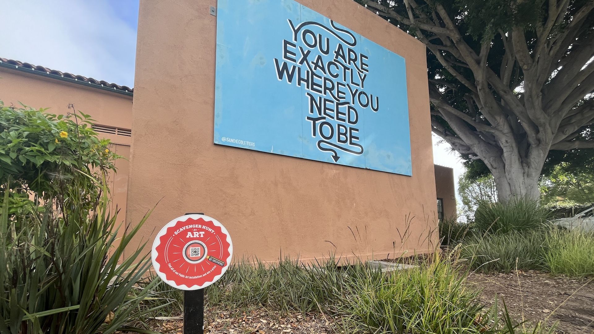 A mural on a wall with a sign for a scavenger hunt with a QR code. 