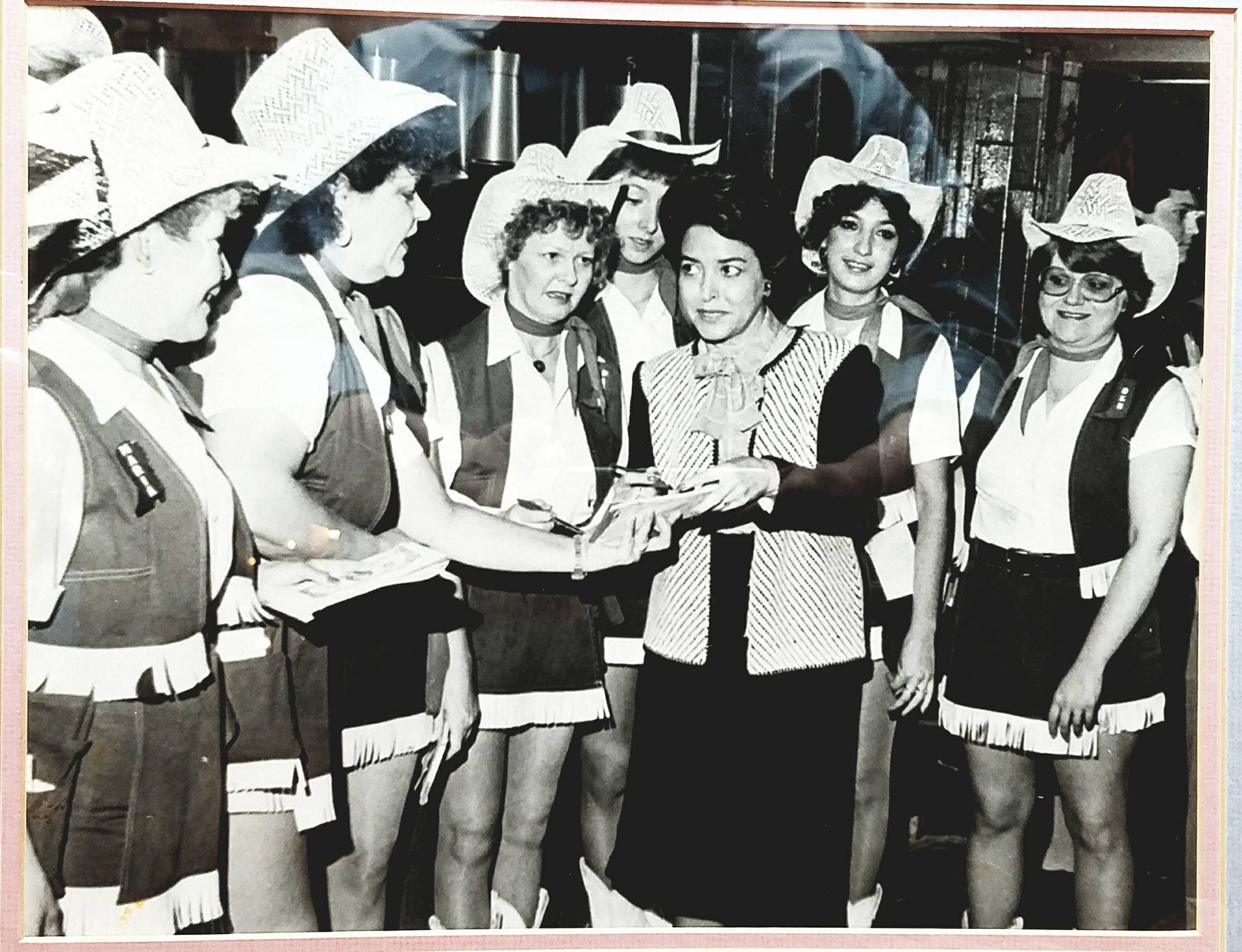 A woman stands in a huddle of women, signing autographs. 