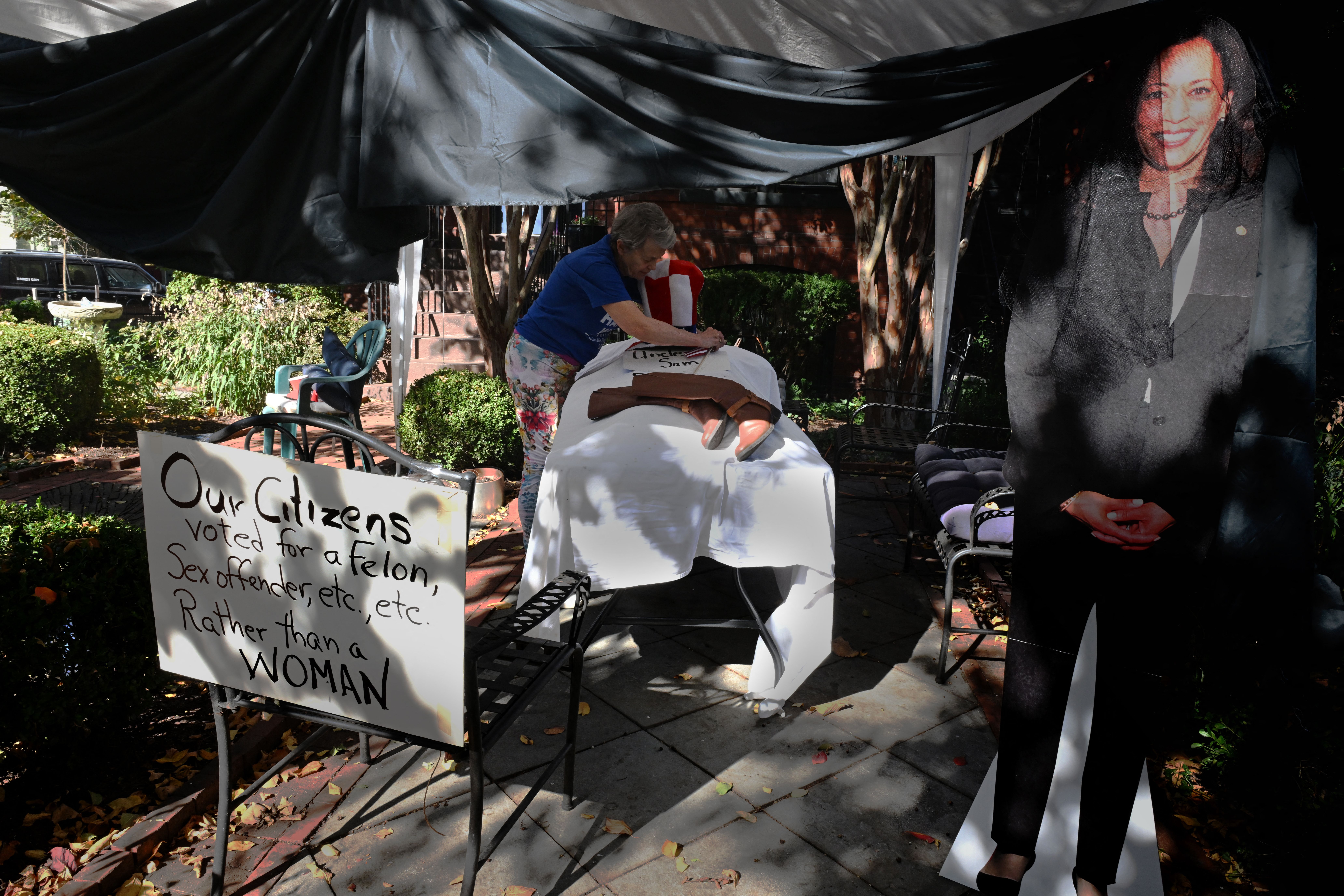 A woman stands in front of a faux gurney with a sign supporting Vice President Harris.