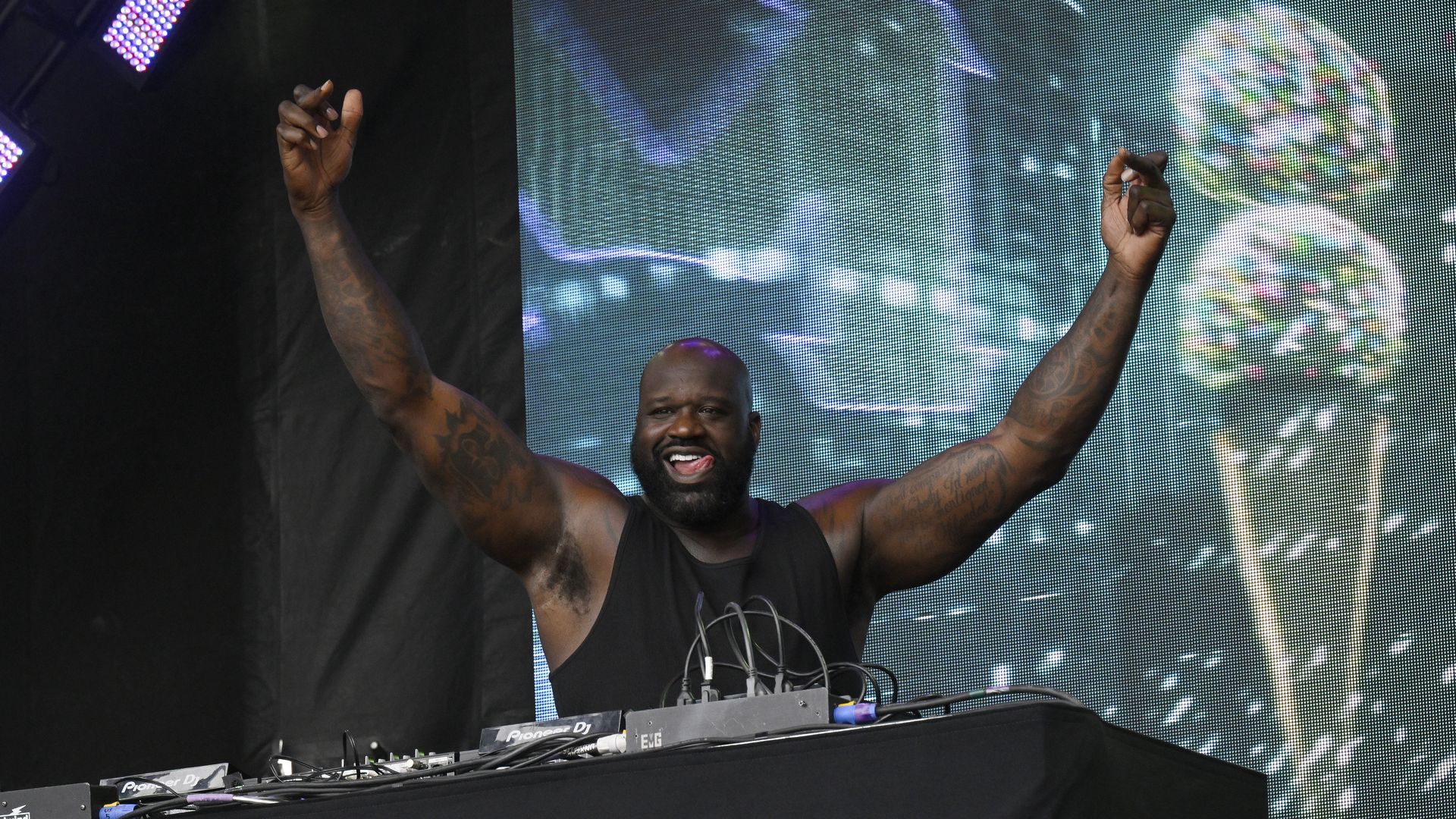 Shaquille O'Neill sticks out his tongue and raises both hands in the air. 