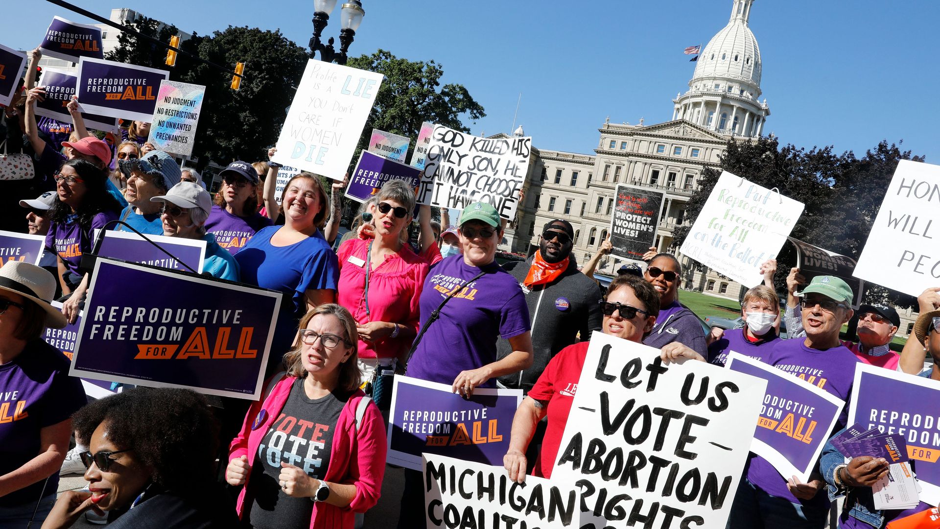 Photo of abortion rights protesters holding up signs in front of the Michigan state capitol