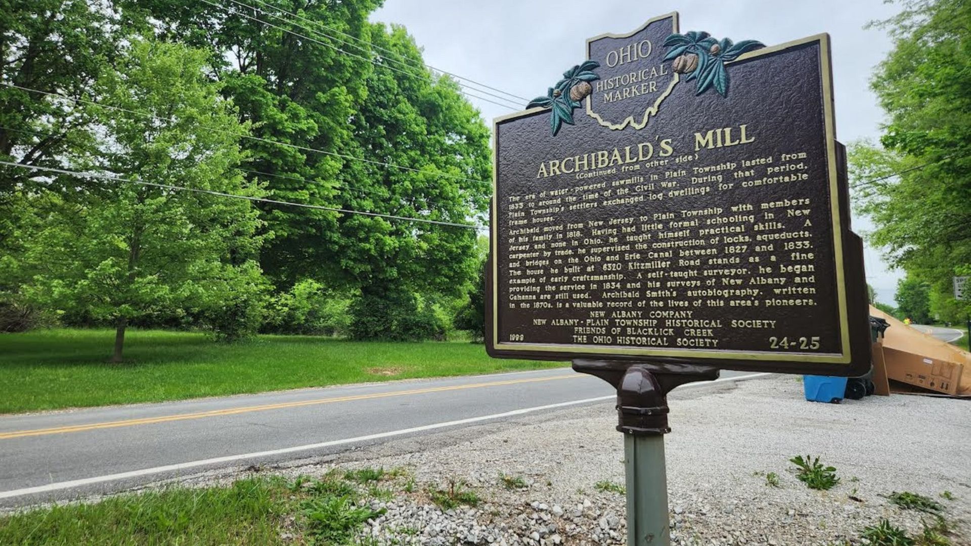 A historical marker for "Archibald's Mill" in front of a road.
