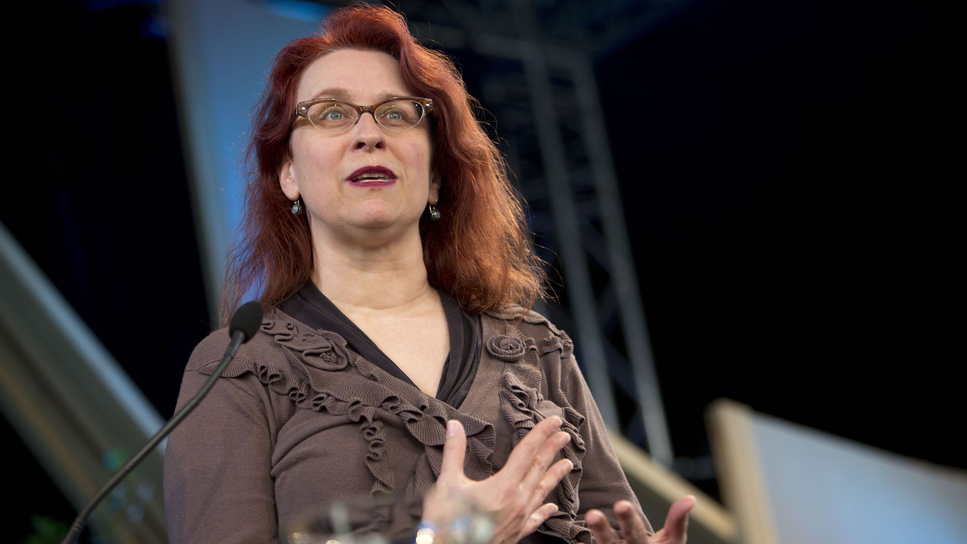 Photo of a woman on stage talking to an audience. 