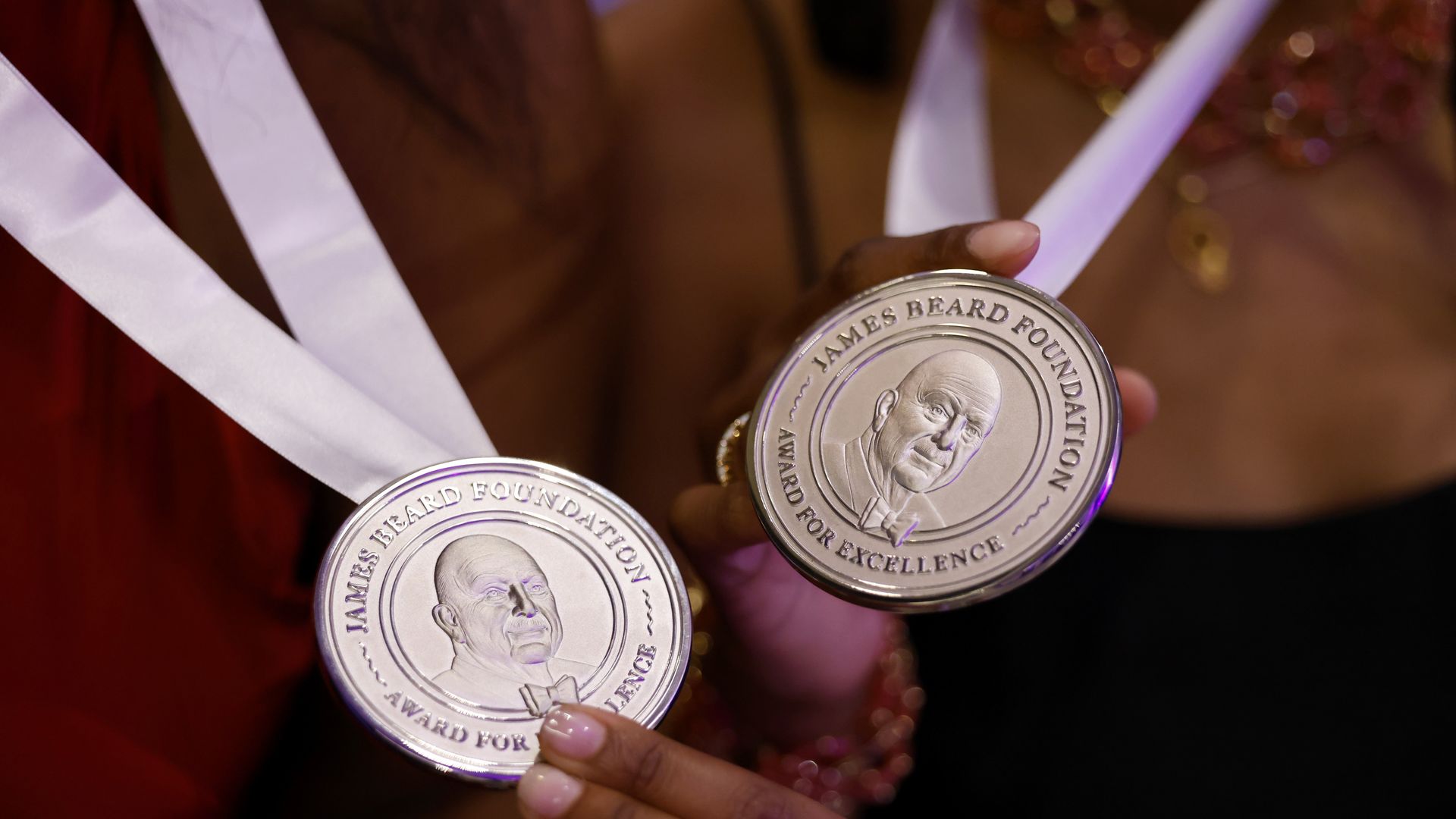 Two people hold out silver medals for James Beard awards. 
