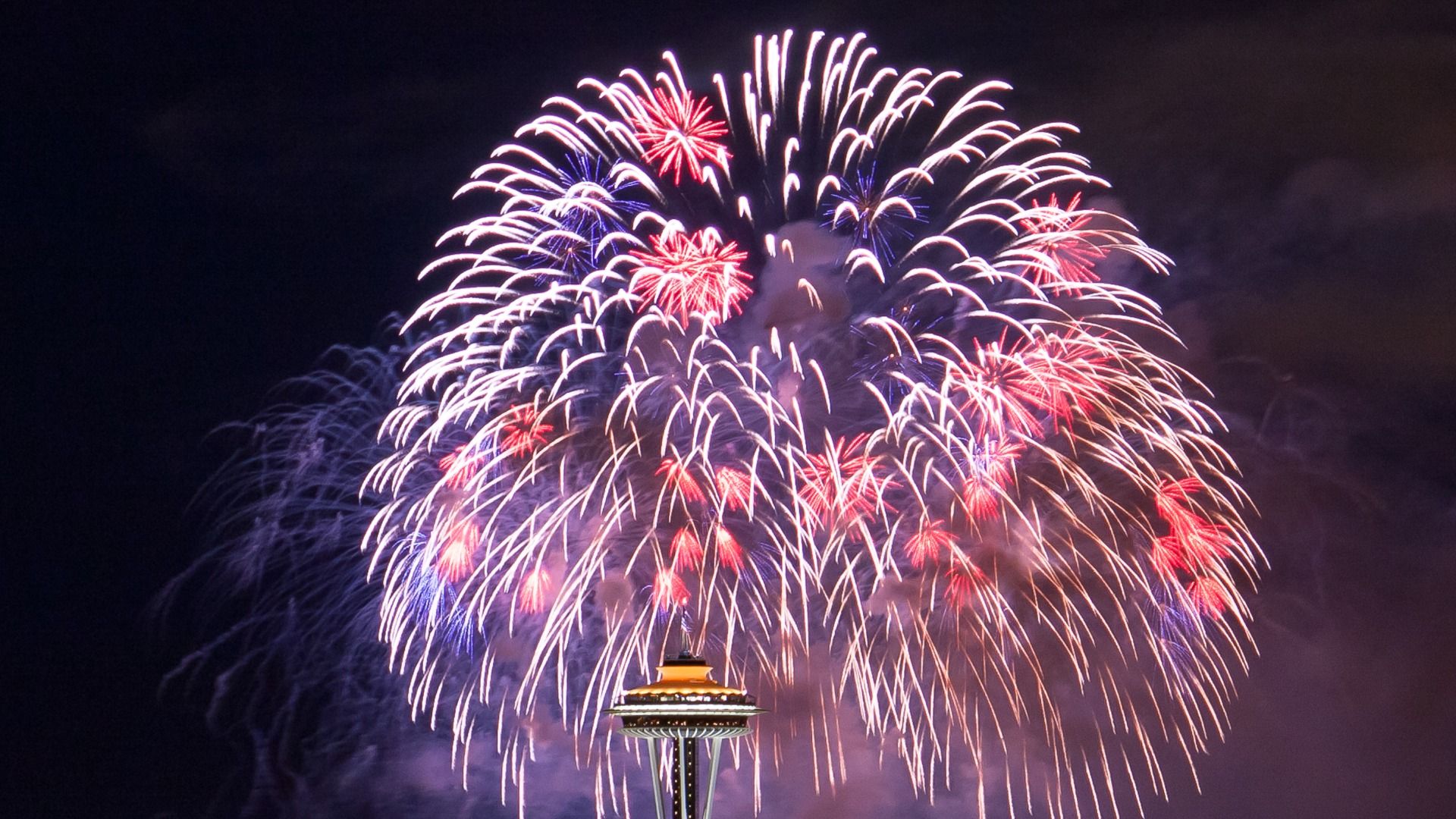 Red, white and blue fireworks explode behind the Space Needle.
