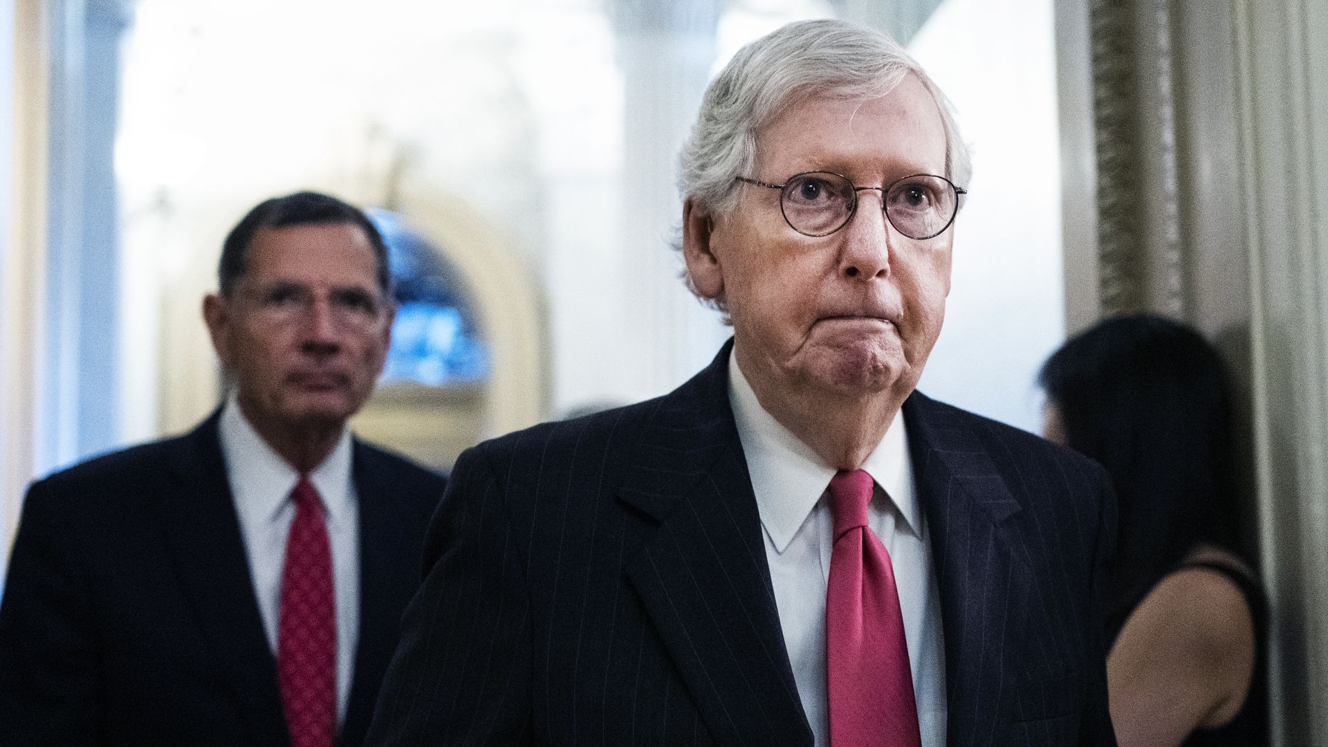 Photo of Mitch McConnell walking in a hall with his lips pursed