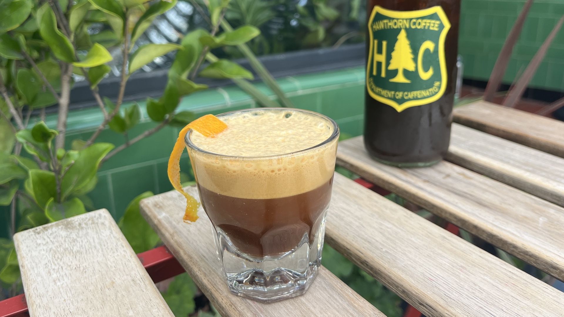 A foamy espresso drink with an orange peel on a wooden table with another iced coffee.