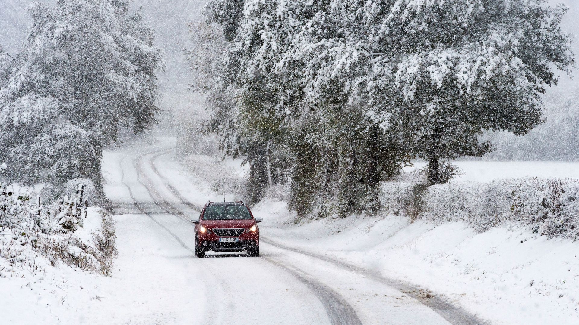 a red car driving on a winding road in snow