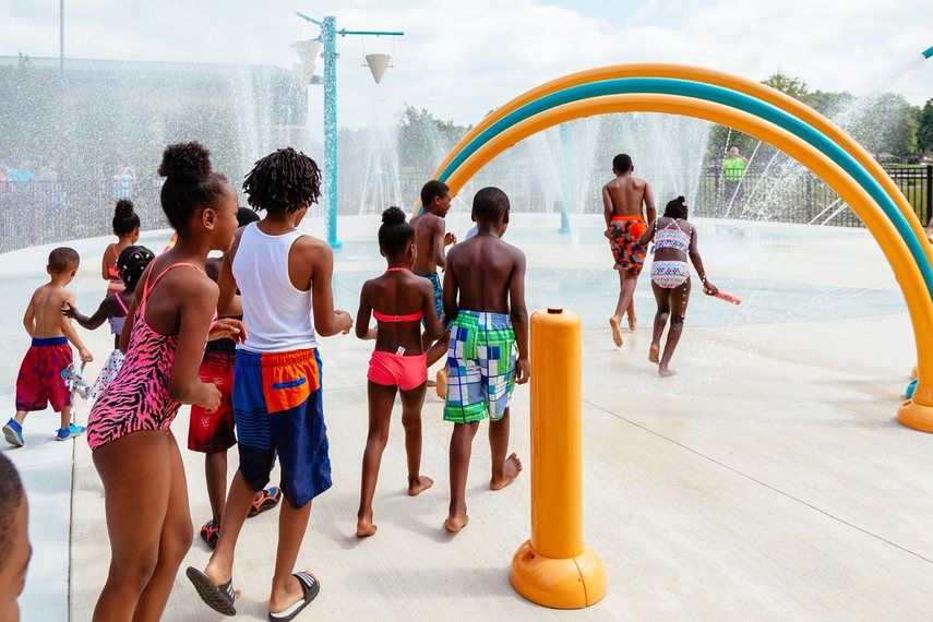 older kids stand in line waiting for their turn to get in a  rainbow splash pad