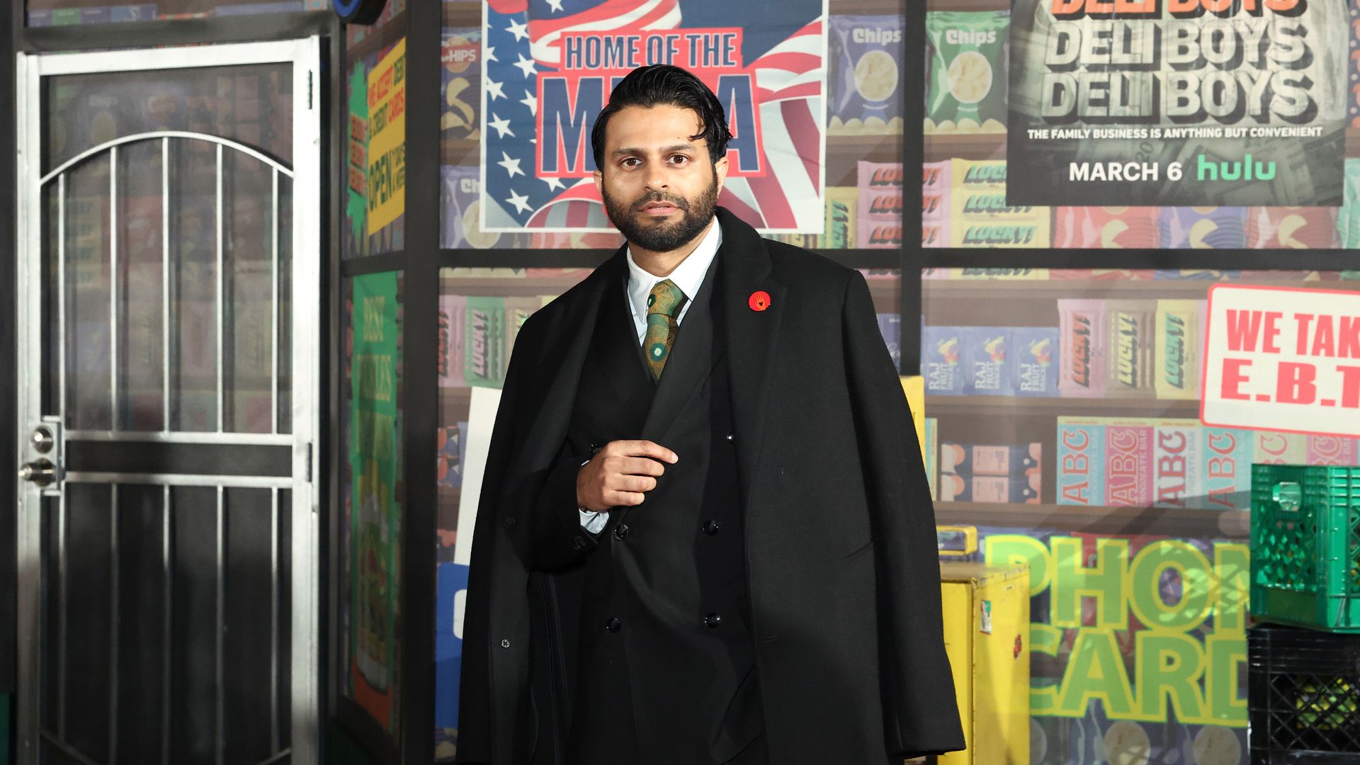 Photo of a man in a suit standing in front of a sign that says "Deli Boys" 