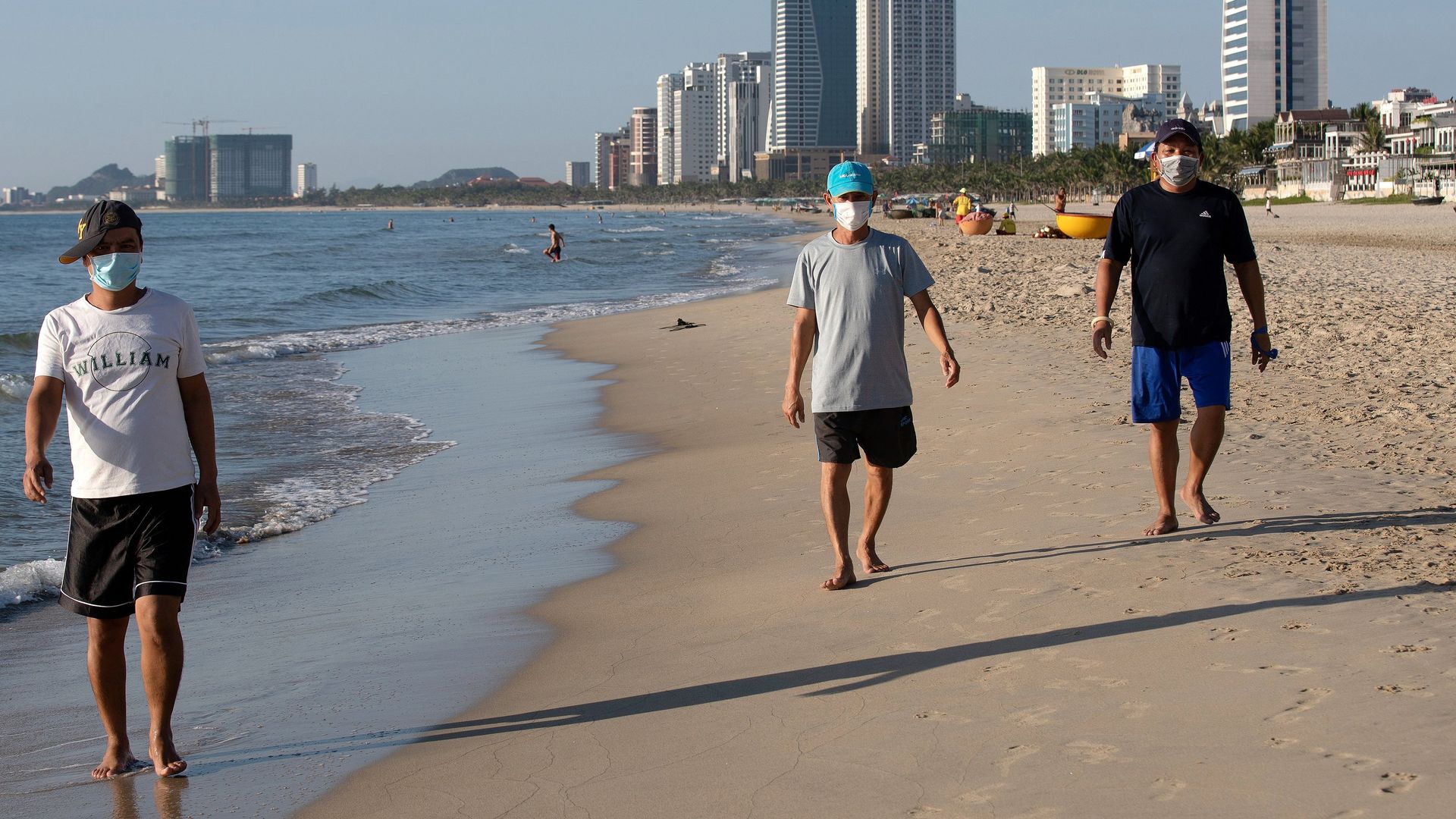 eople wearing protective face masks walk along My Khe beach in Danang on July 28