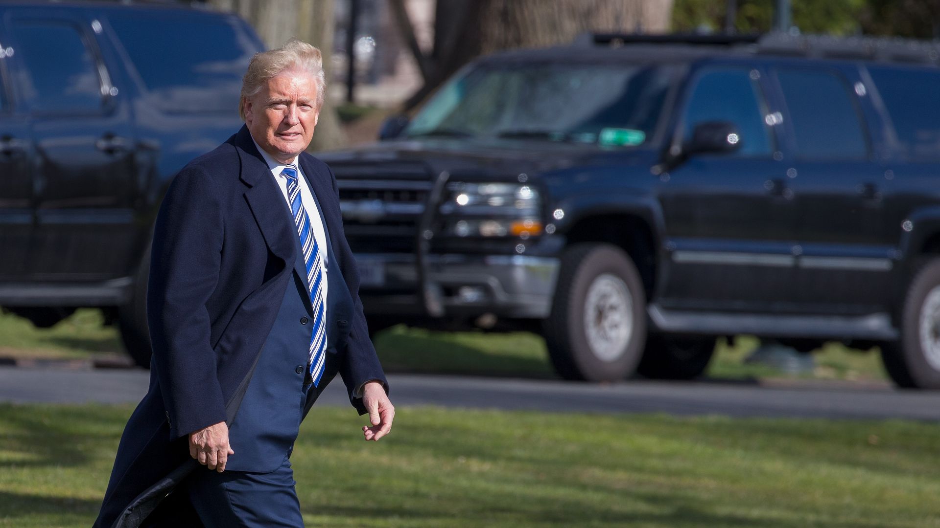 Donald Trump walking outside in a navy blue suit and coat