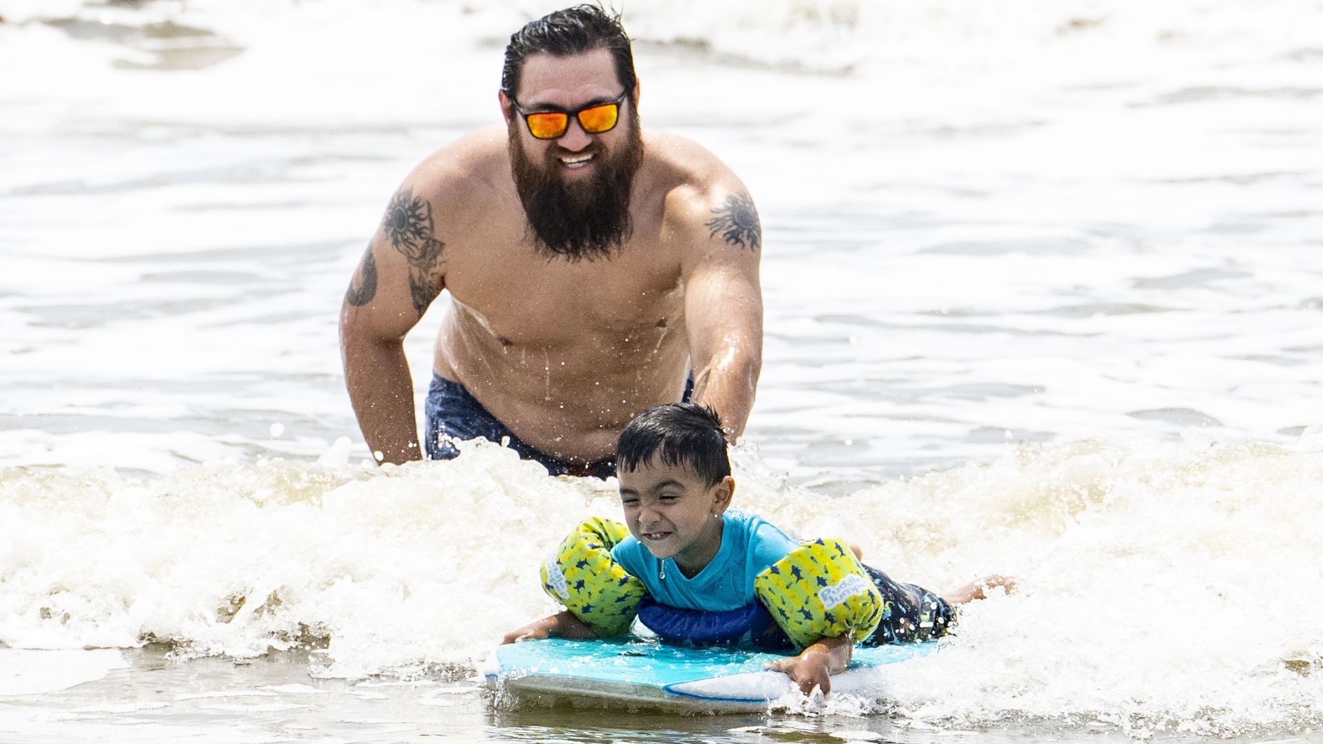 A father pushes his son on a boogie board in the water in Galveston