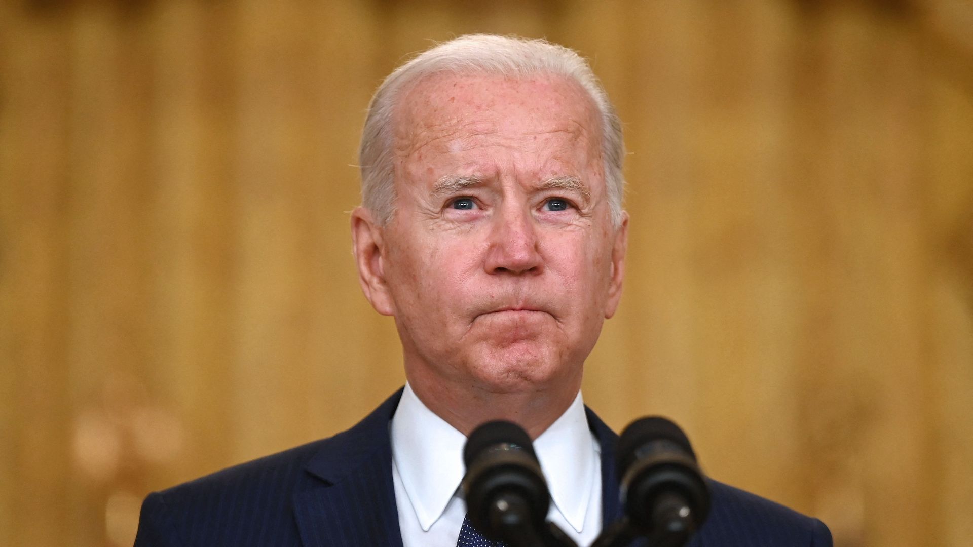President Biden sands in front of a microphone with pursed lips.