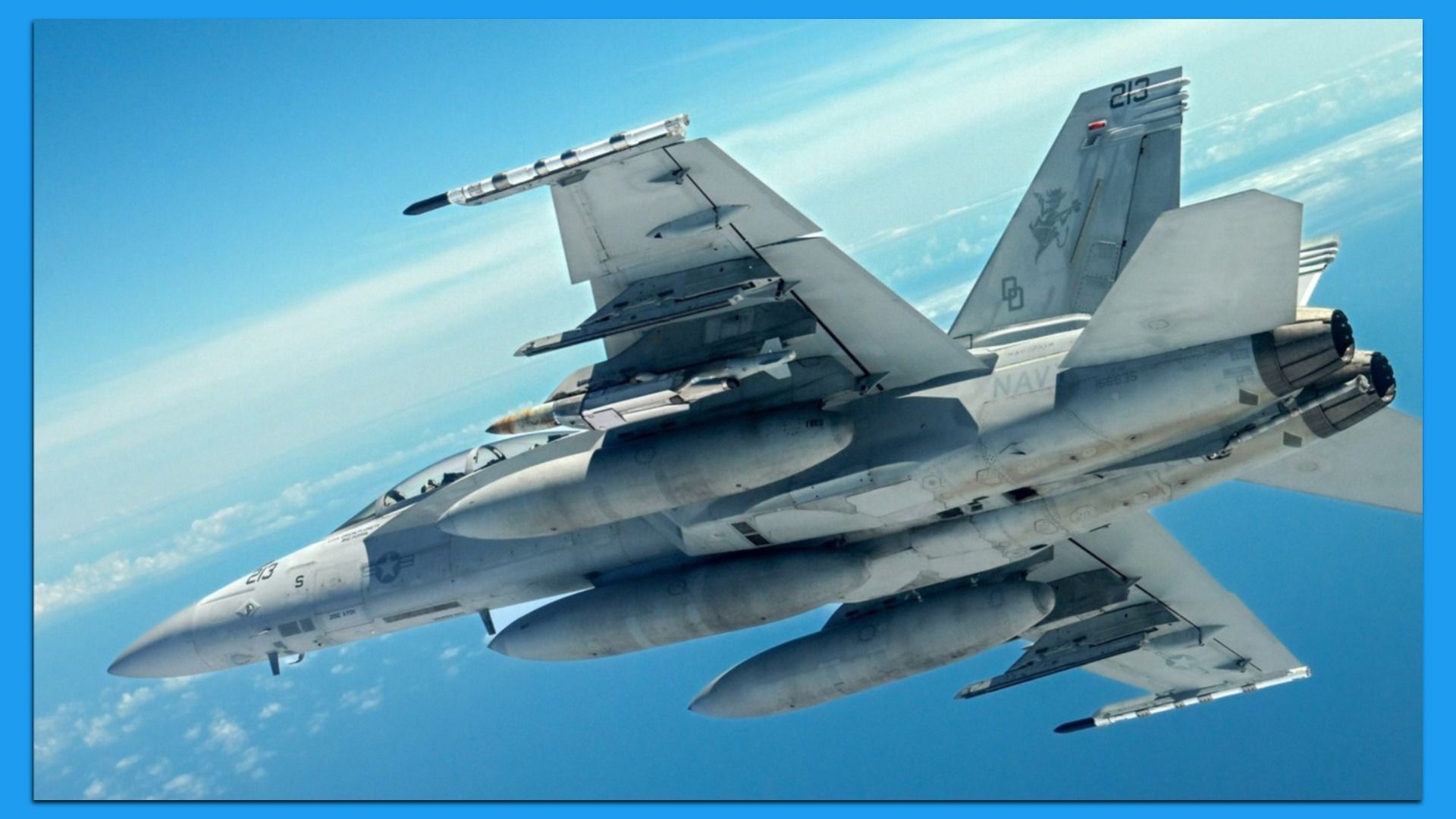 The belly of a fighter jet is seen against blue skies. It is carrying munitions and fuel tanks.