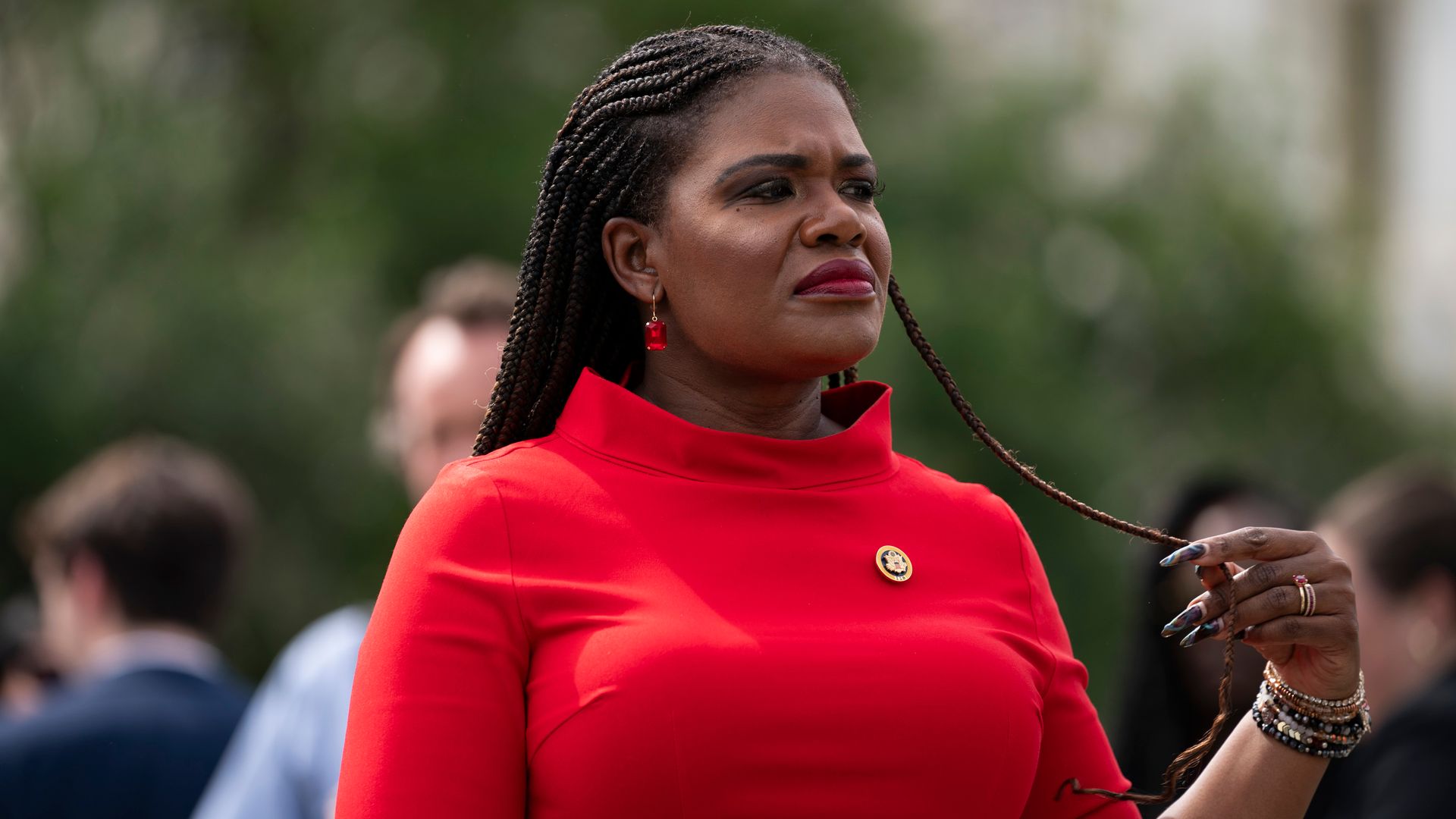Rep. Cori Bush, wearing a red dress and holding a strand of her hair outdoors.