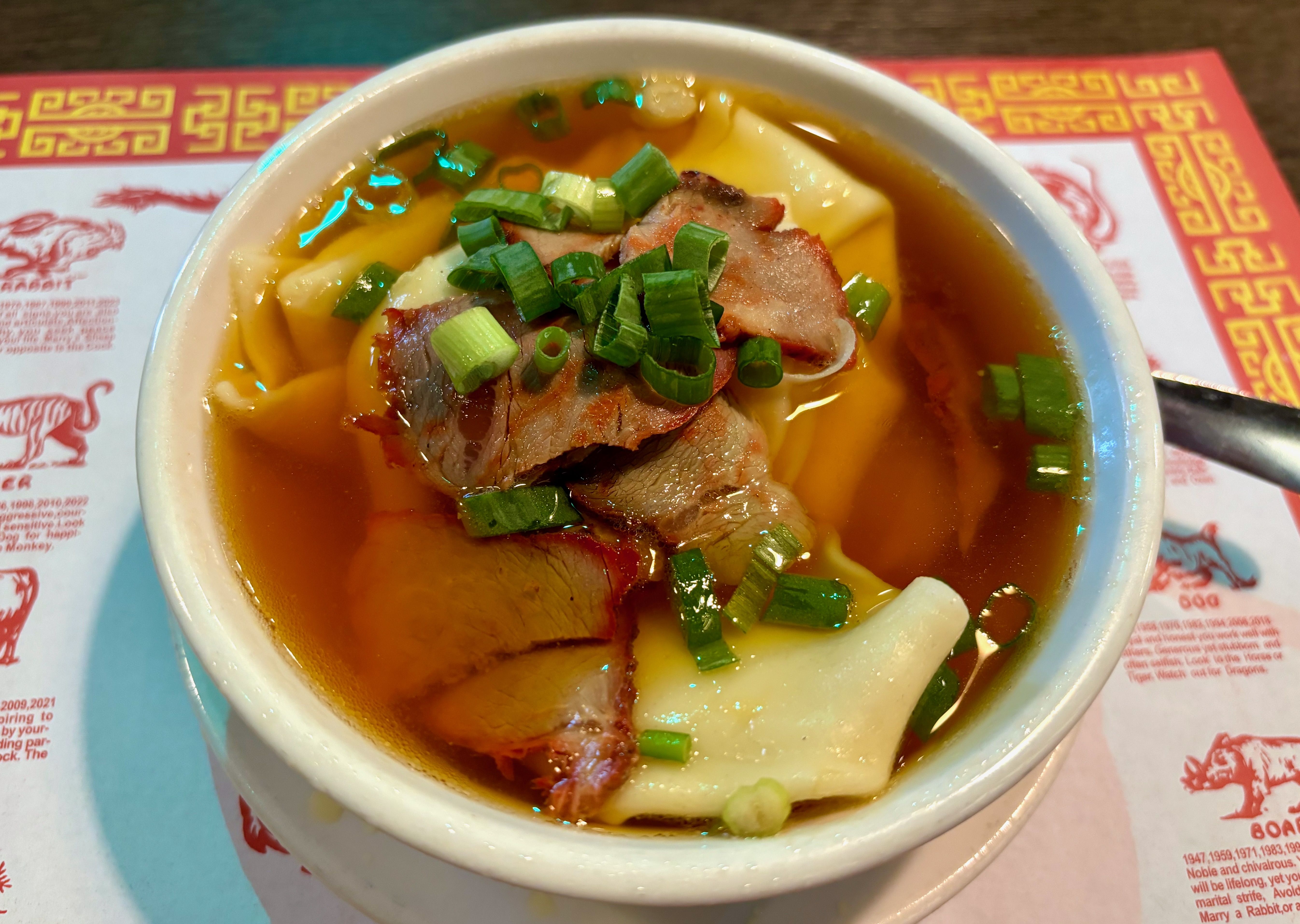 A bowl of wonton soup with strips of pork and scallions on top
