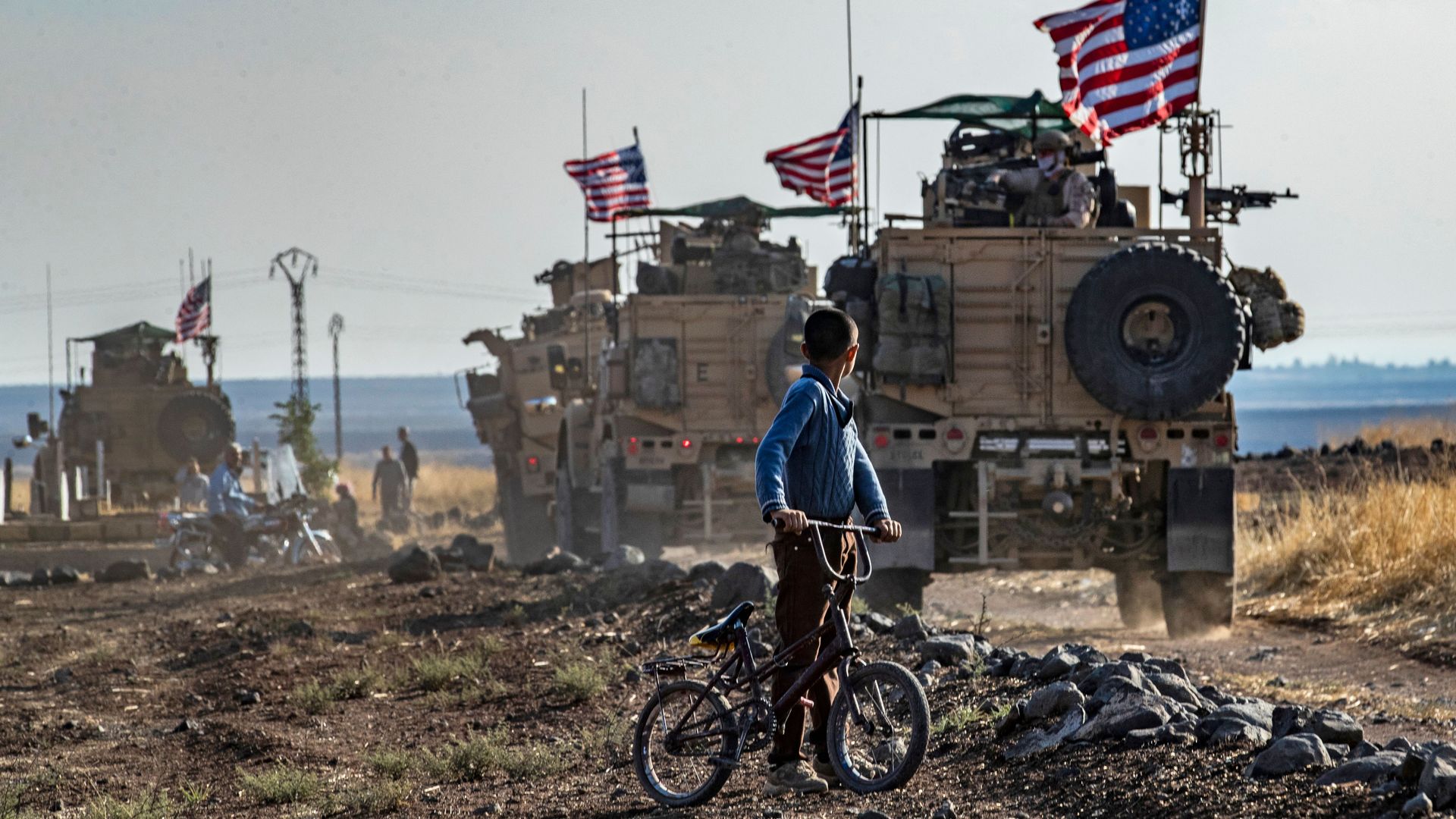 A boy watches a U.S. convoy on patrol in Syria