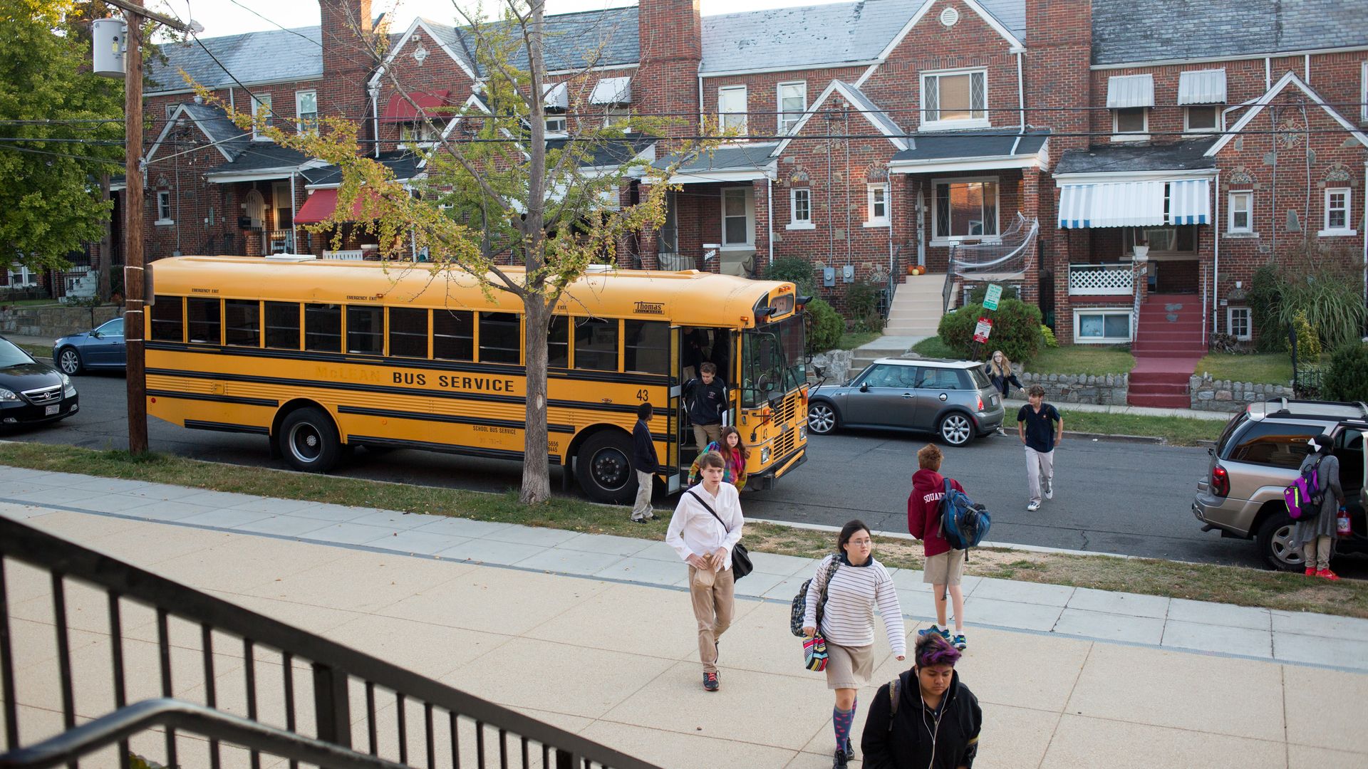 Students get off of a school bus and walk into the school building.