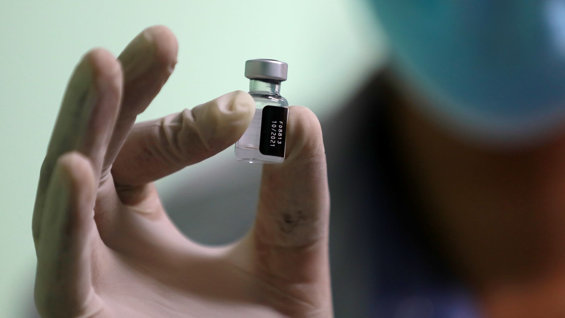 A photo of a gloved hand holding a vile of a dose of the Pfizer vaccine
